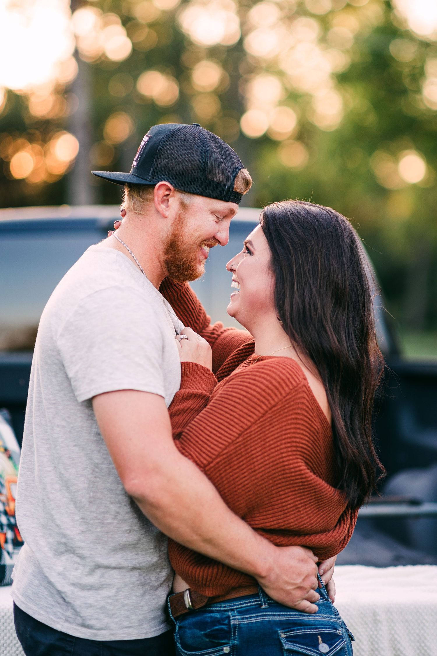 A happy couple embraces and smiles at each other near a pickup truck during a warm sunset.
