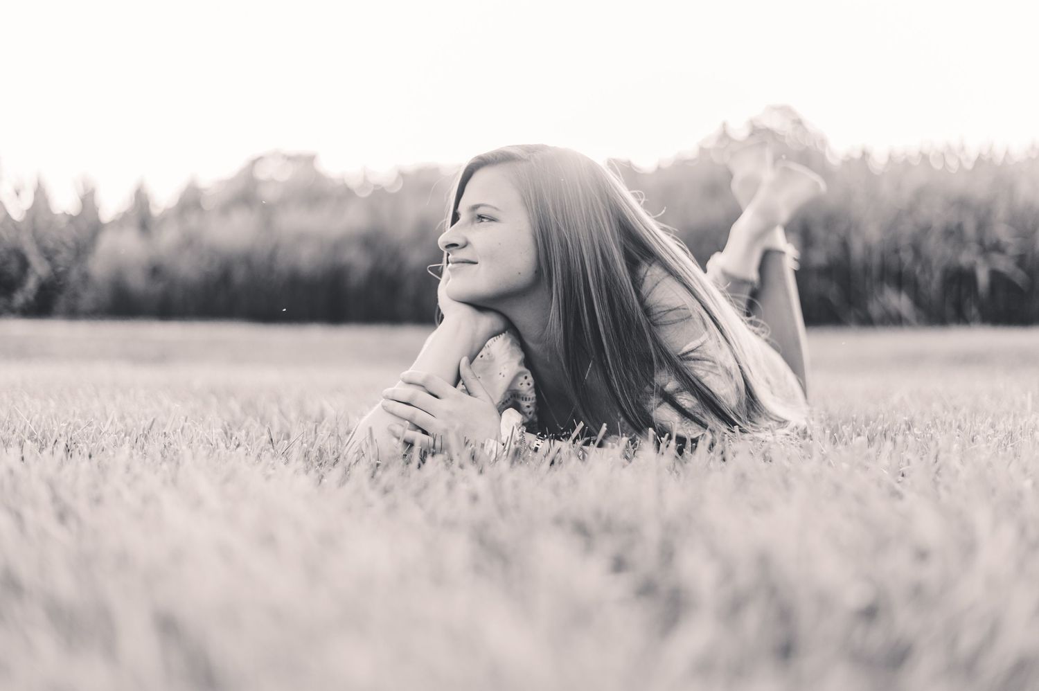Black and white photo of a teenage girl lying in a grassy field, smiling dreamily outdoors.