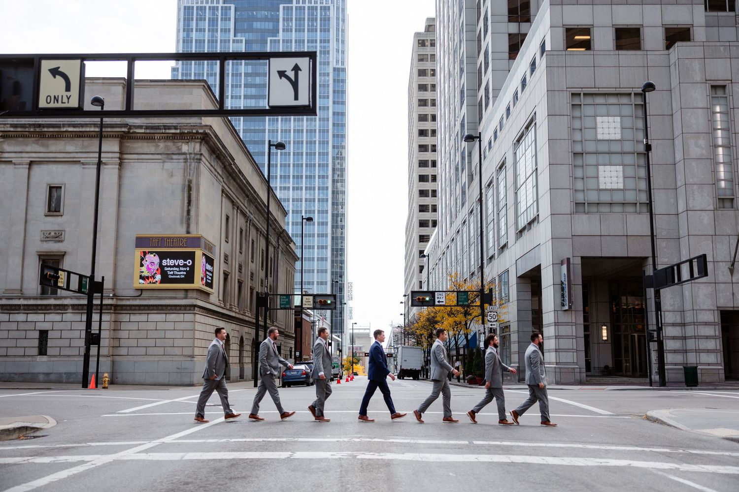 Groomsmen in gray suits cross a busy downtown Cincinnati street intersection in a Beatles Abbey Road style photo.