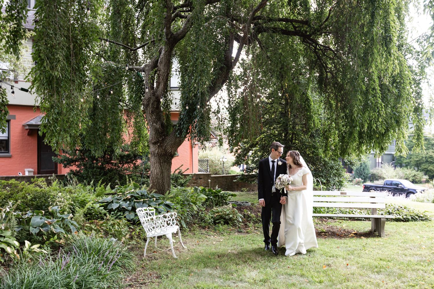 Bride and groom sharing quiet moment under weeping willow tree in garden setting.