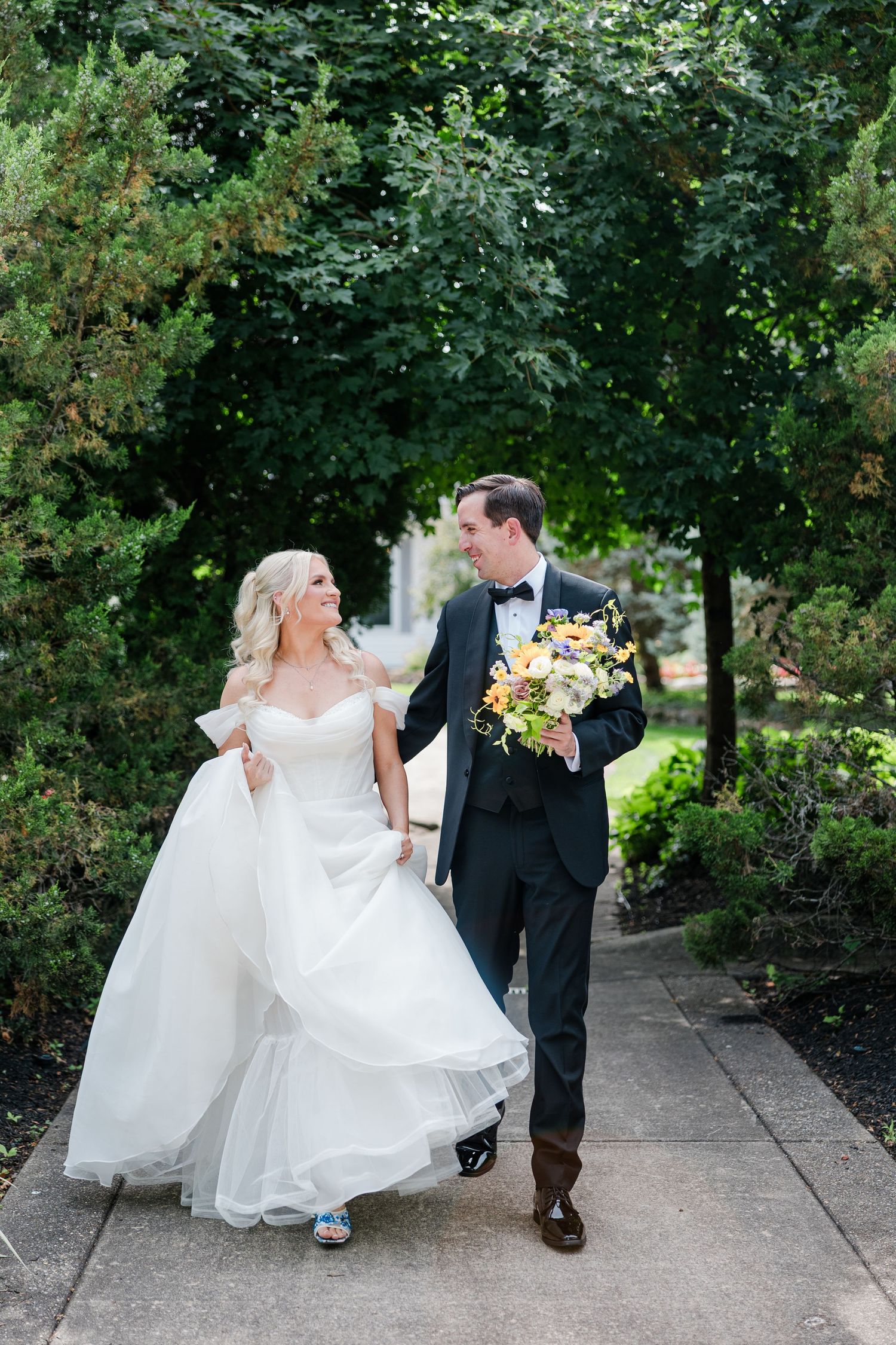 Bride and groom walking hand in hand through a garden path with colorful bouquet at the manor house.