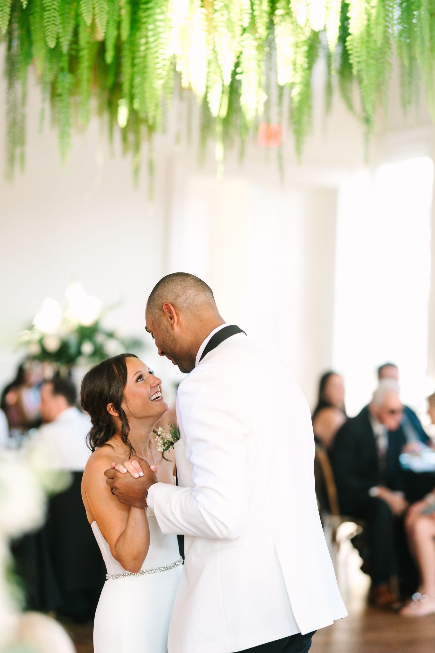 Bride and groom sharing their first dance beneath lush hanging ferns at their wedding reception at the alcove by madtree.