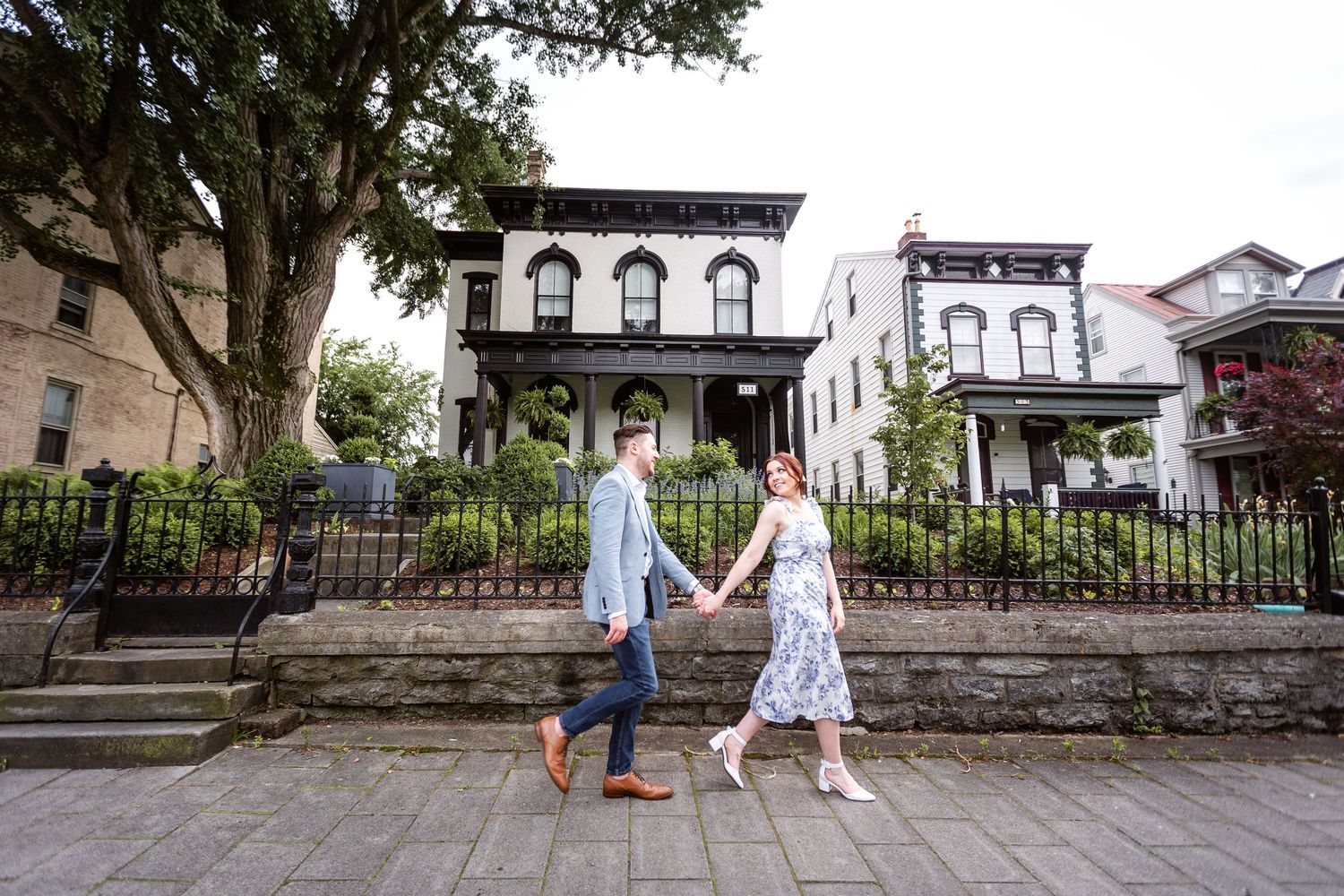 Couple walking hand in hand past historic Victorian homes on a charming tree-lined brick sidewalk.