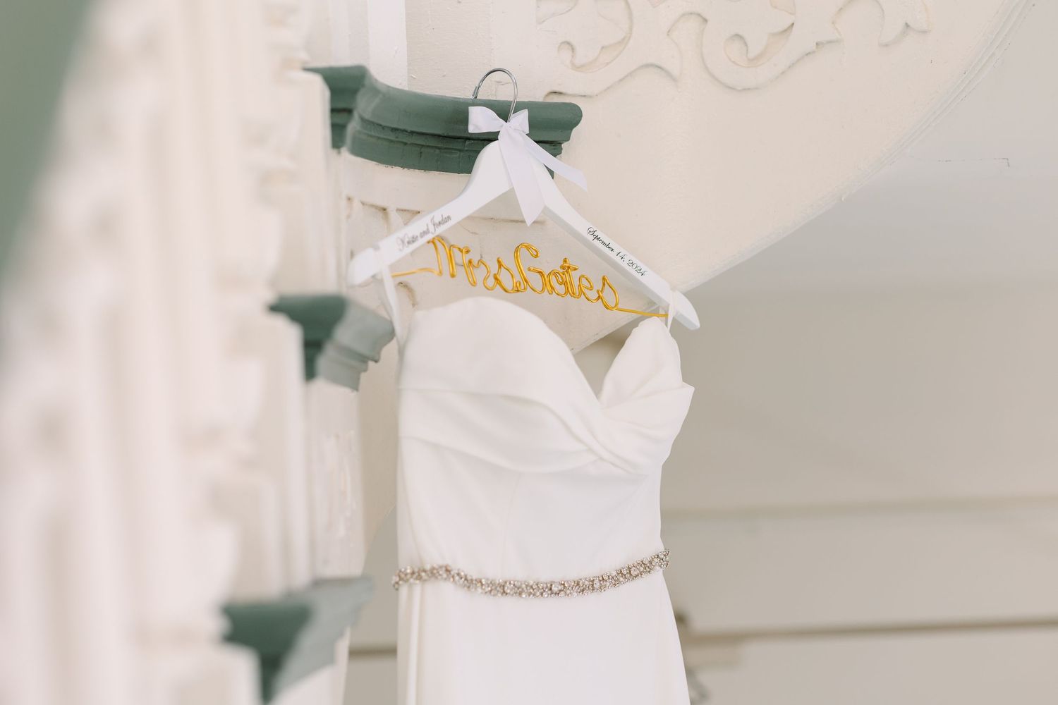 White wedding dress on a personalized hanger displayed on an elegant white pillar.