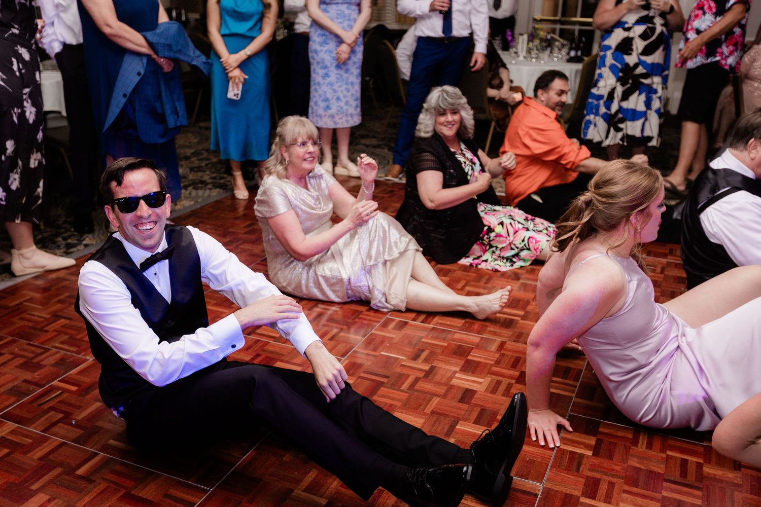 Wedding guests sitting and sliding on a herringbone dance floor laughing during a lively reception celebration at the Manor House.