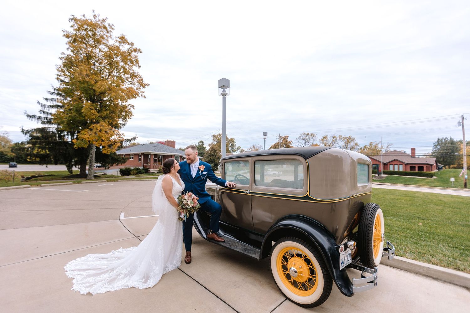 Bride and groom posing with a vintage brown antique car on their wedding day.