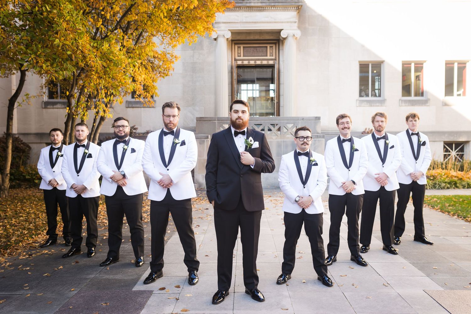 Groom in black tuxedo poses with groomsmen in white jackets outside the Cincinnati Art Museum.