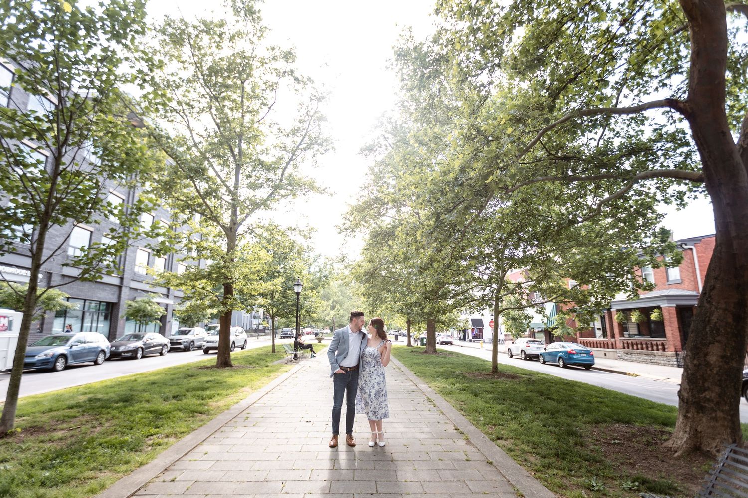 Couple walking hand in hand down a tree-lined brick sidewalk in a charming urban neighborhood setting.