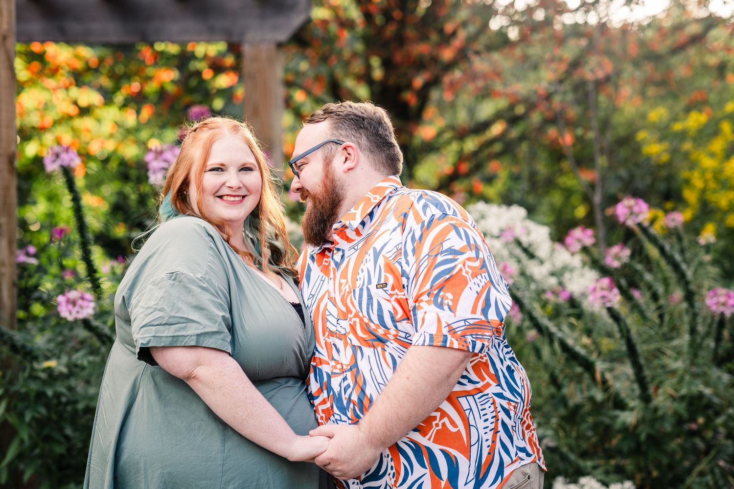 Happy couple embracing and laughing in a colorful flower garden at sunset.