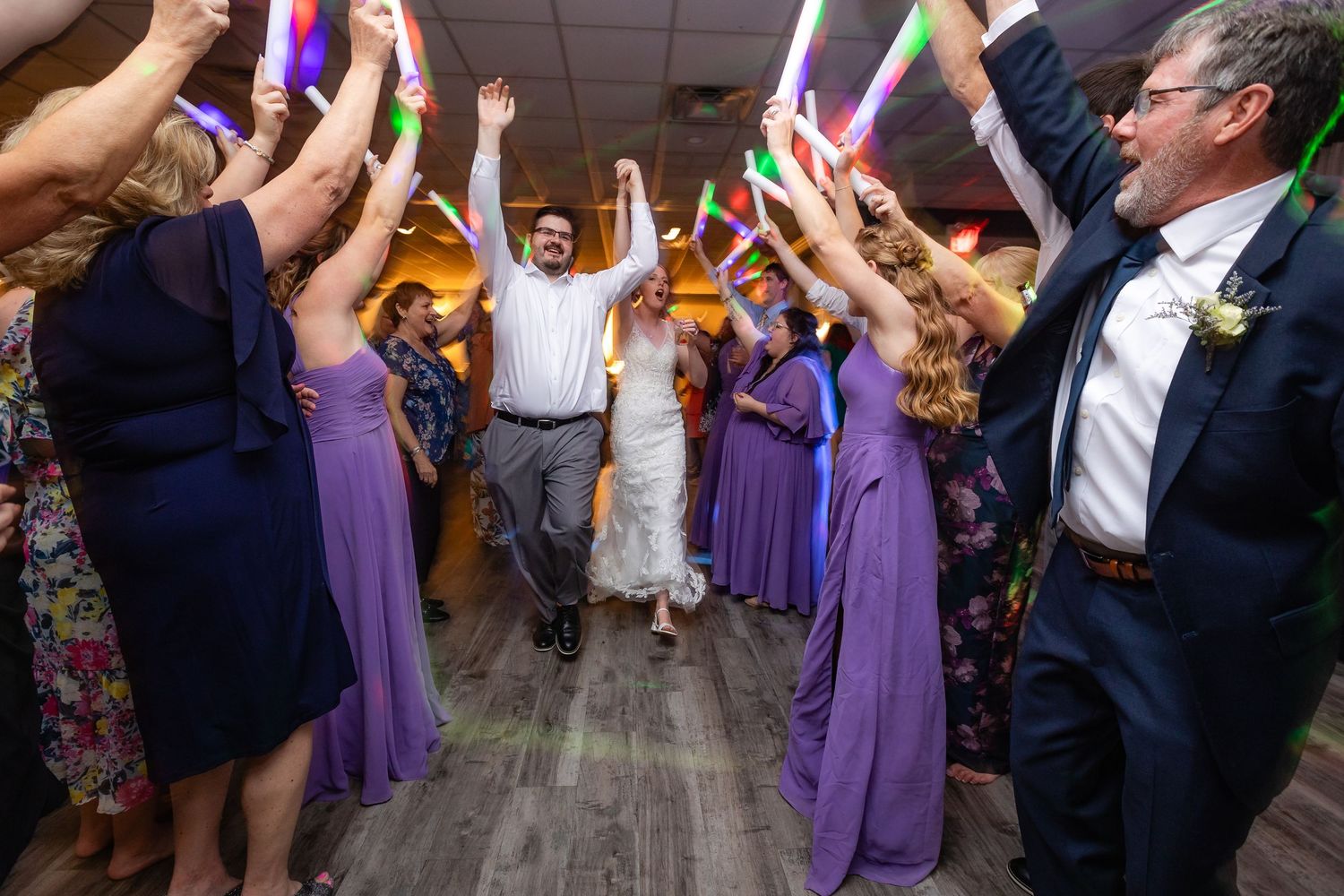 Bride and groom dance through a tunnel of glowing foam sticks held by guests at a wedding reception.