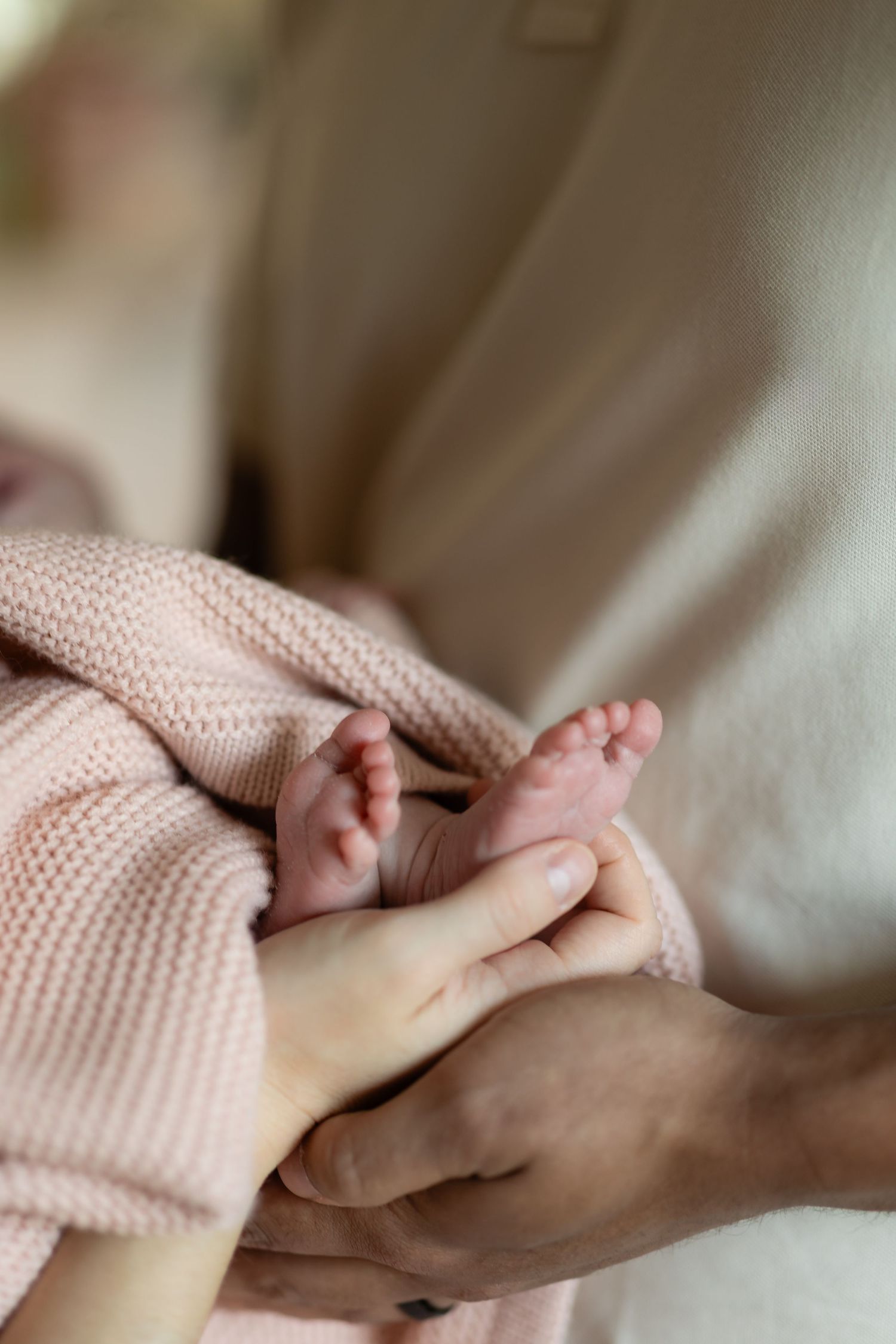 Close-up of a newborns tiny feet wrapped in a pink knit blanket cradled in an adults hands.
