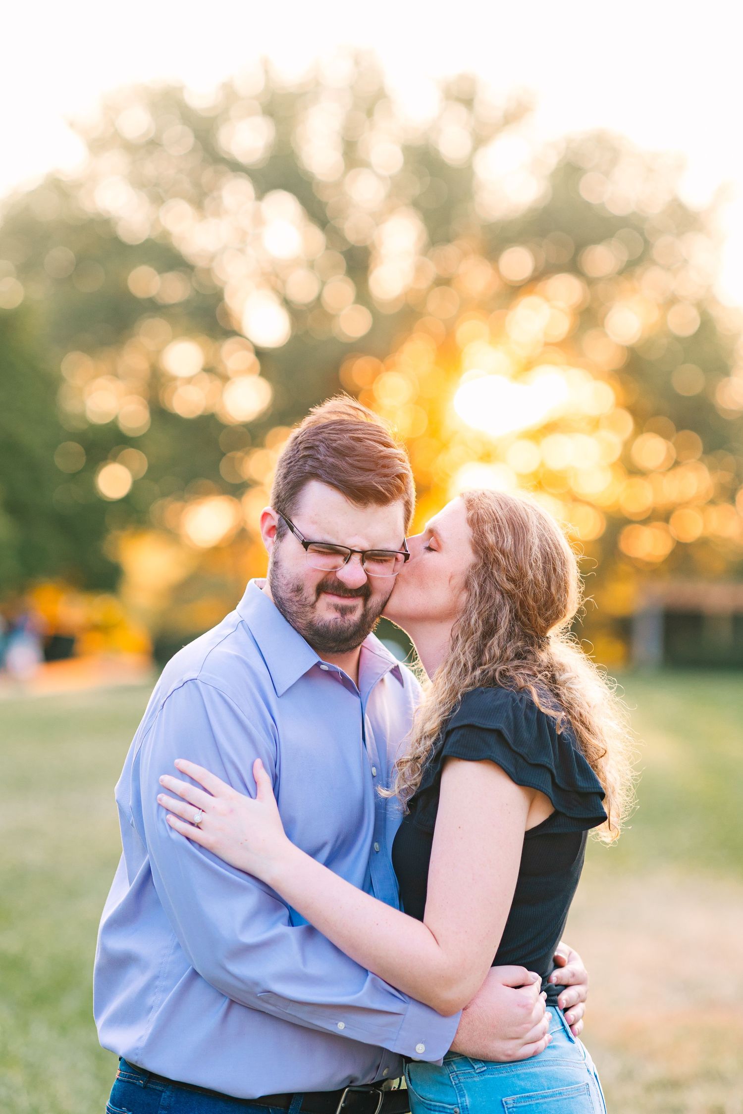 Woman kissing mans cheek during a golden sunset engagement photo outdoors.