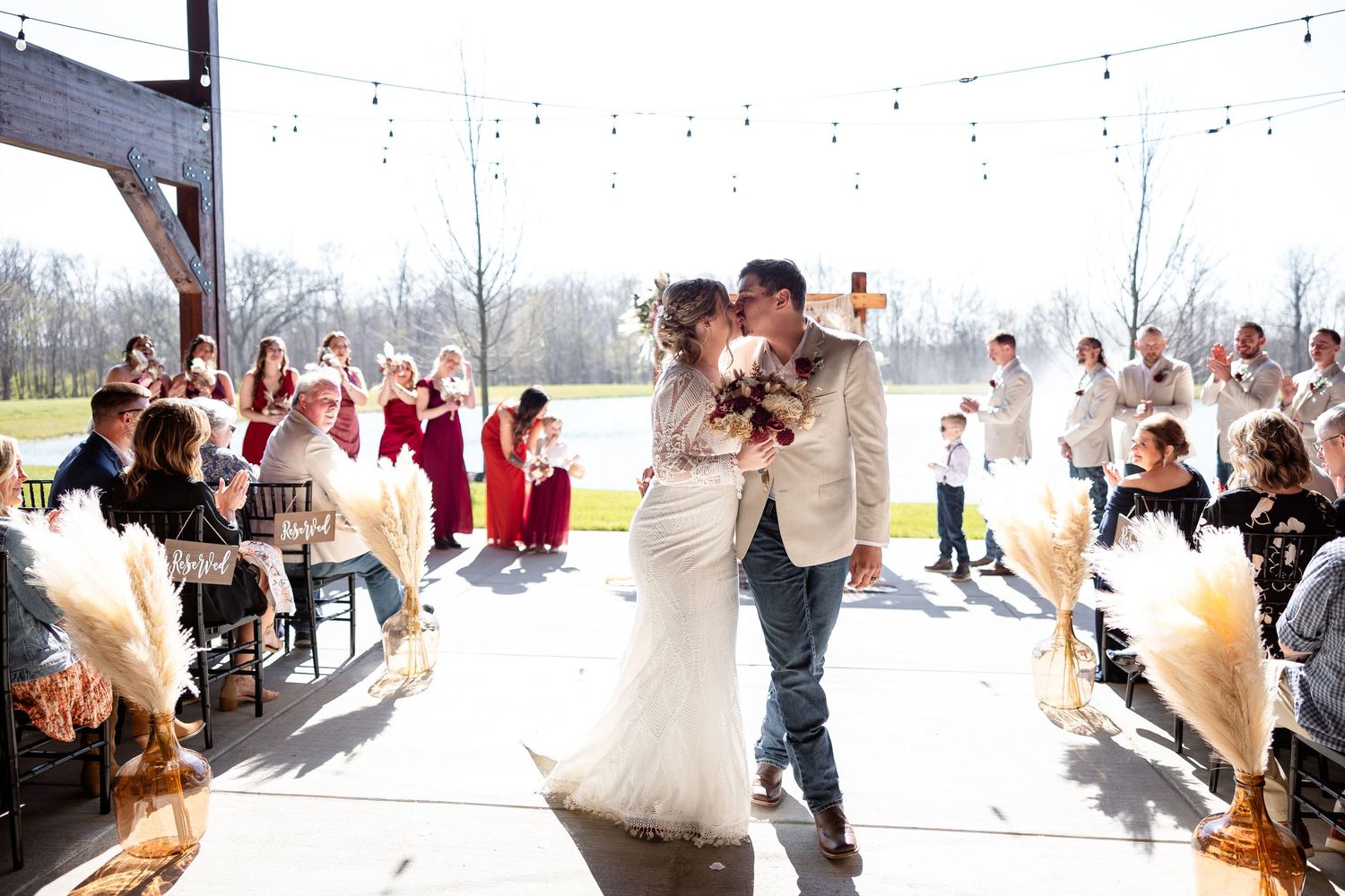 Bride and groom share first kiss at outdoor wedding ceremony with guests and string lights at Hanover Reserve.