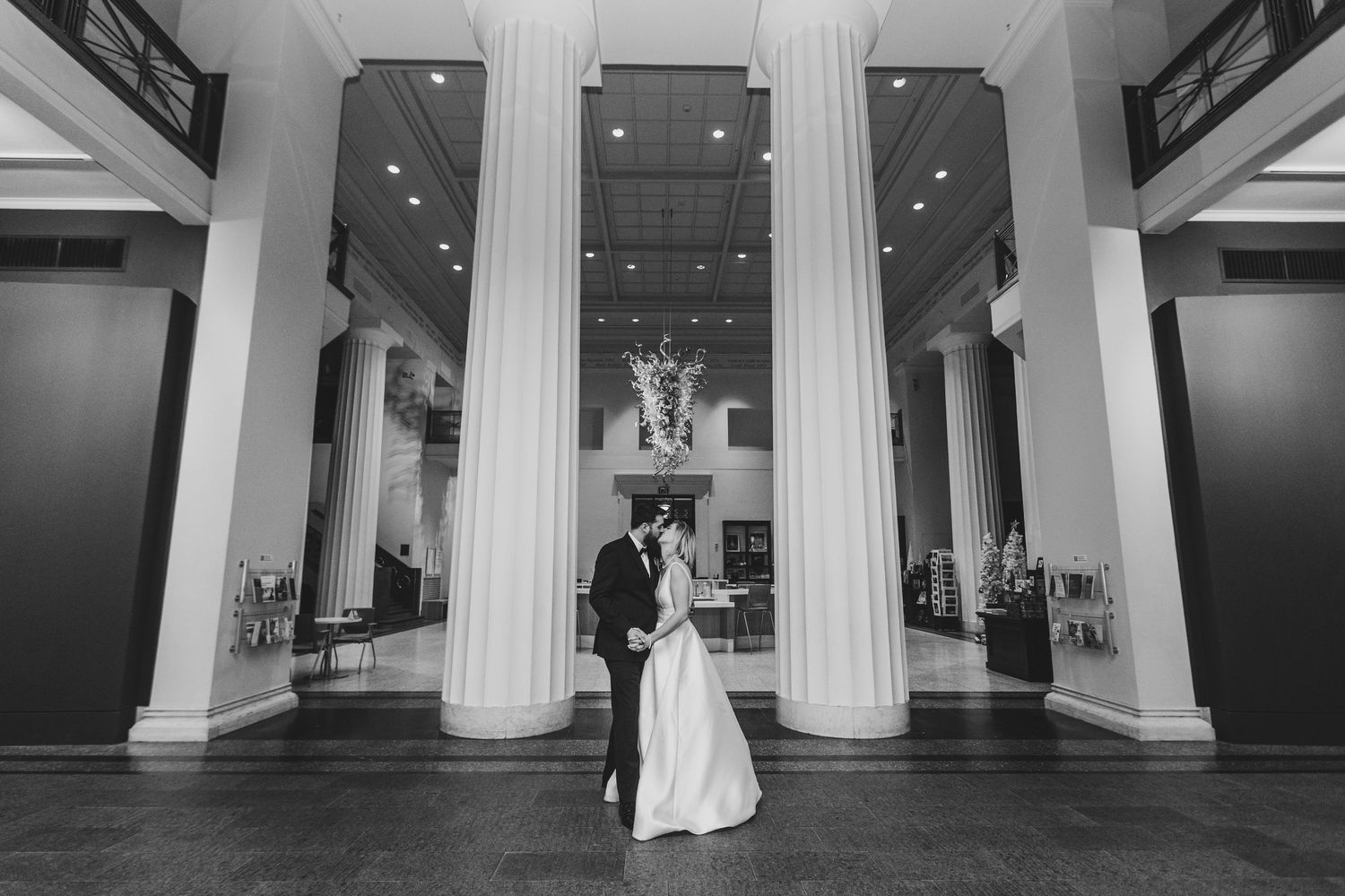 Black and white photo of bride and groom embracing between grand white columns at The Cincinnati Art Museum.