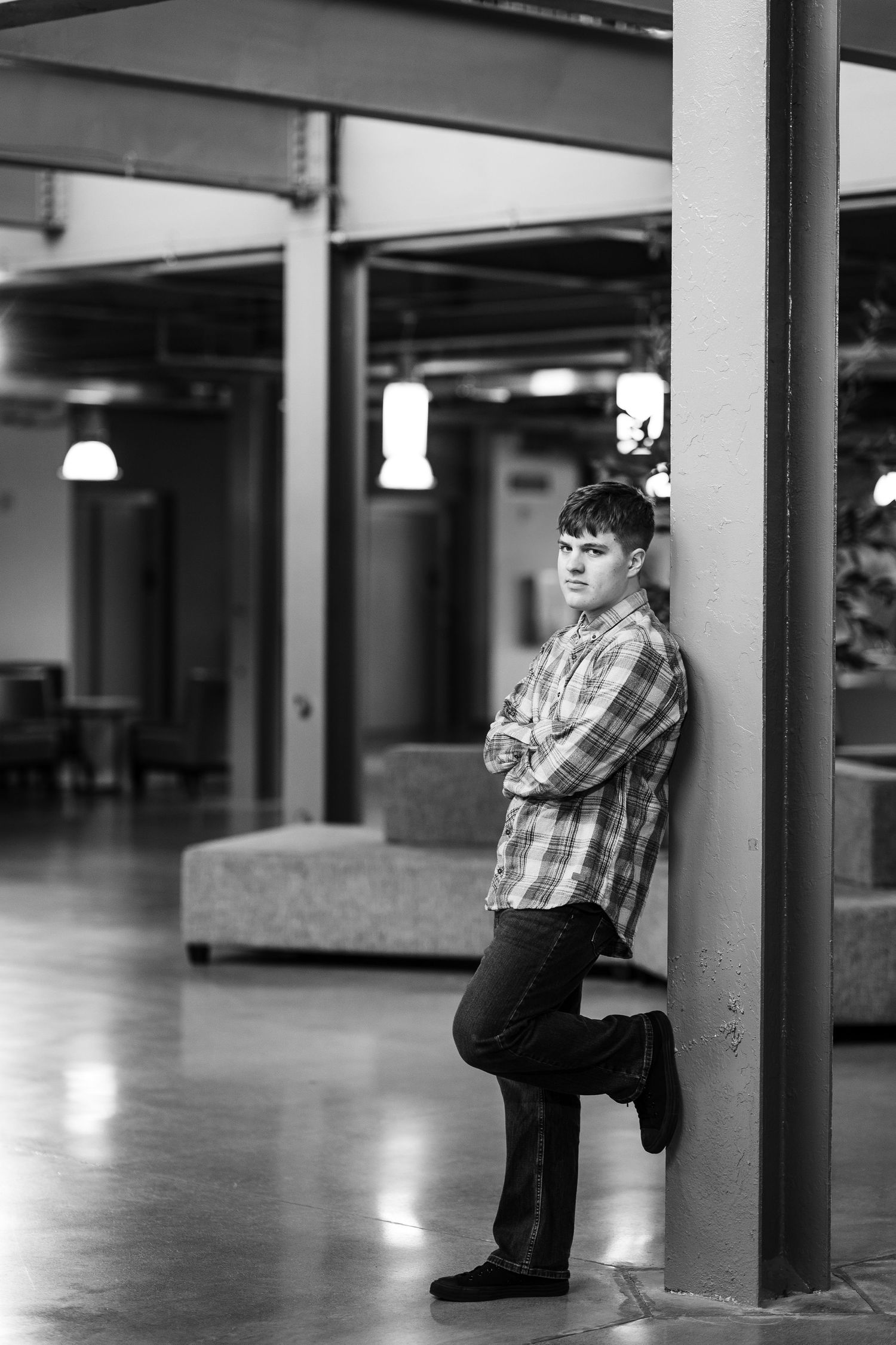 Young man leaning against a pillar with arms crossed in a modern indoor space, black and white portrait.