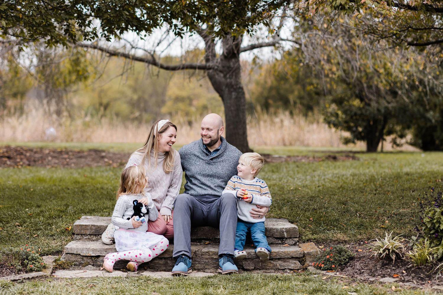 Happy family of four sitting on stone steps under a tree in French Park.
