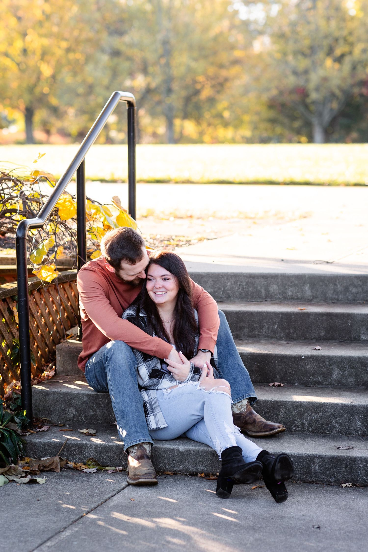 Couple sitting closely on outdoor stone steps surrounded by fall foliage.