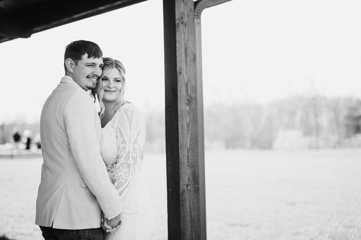 Black and white photo of smiling bride and groom embracing under wooden structure at Hanover Reserve.