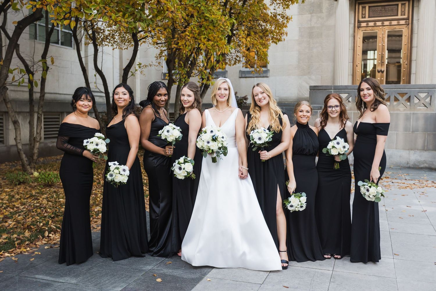 Bride in white gown poses with eight bridesmaids in black dresses holding white bouquets at the Cincinnati Art Museum.