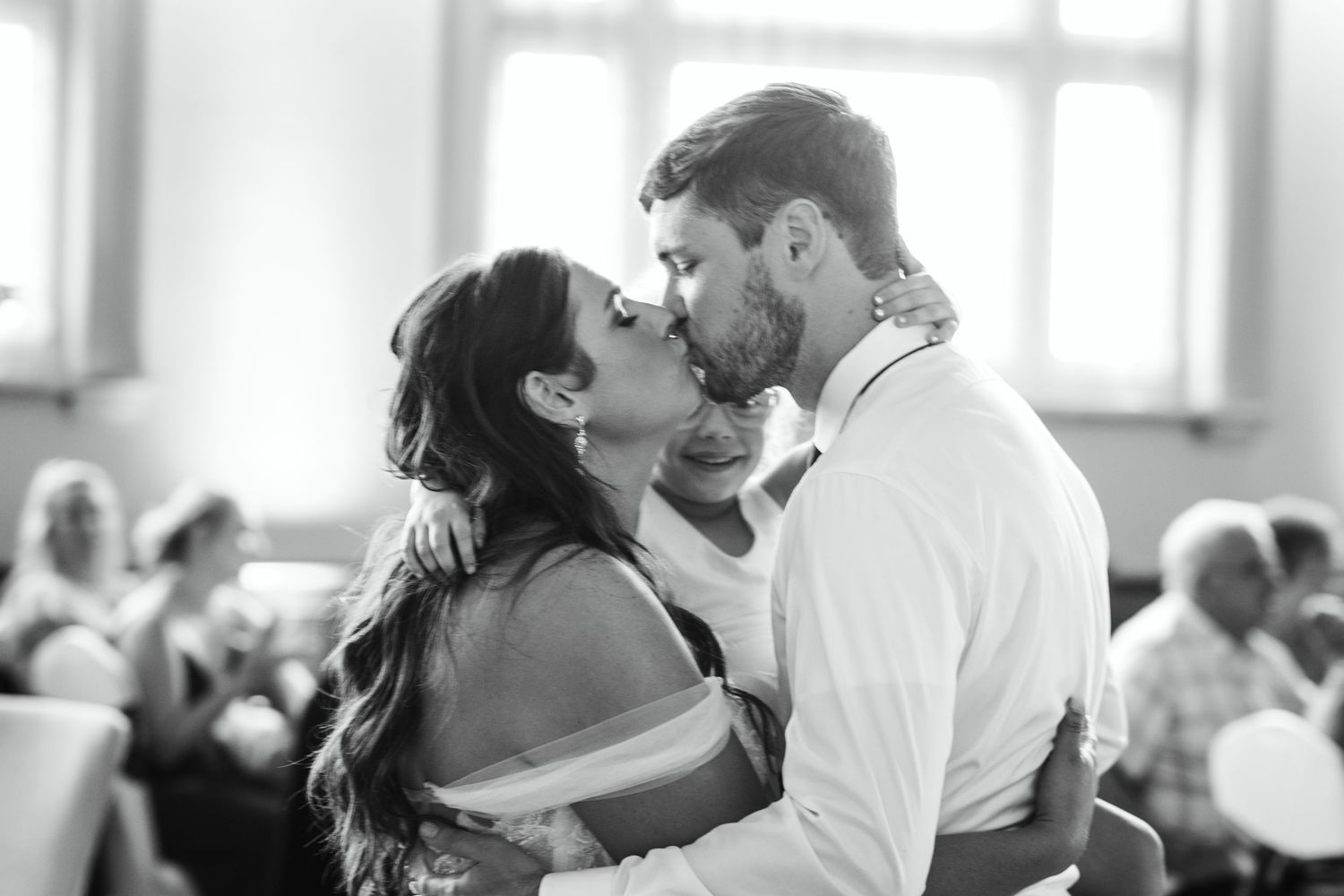 Black and white photo of bride and groom sharing passionate first kiss during wedding reception dance.