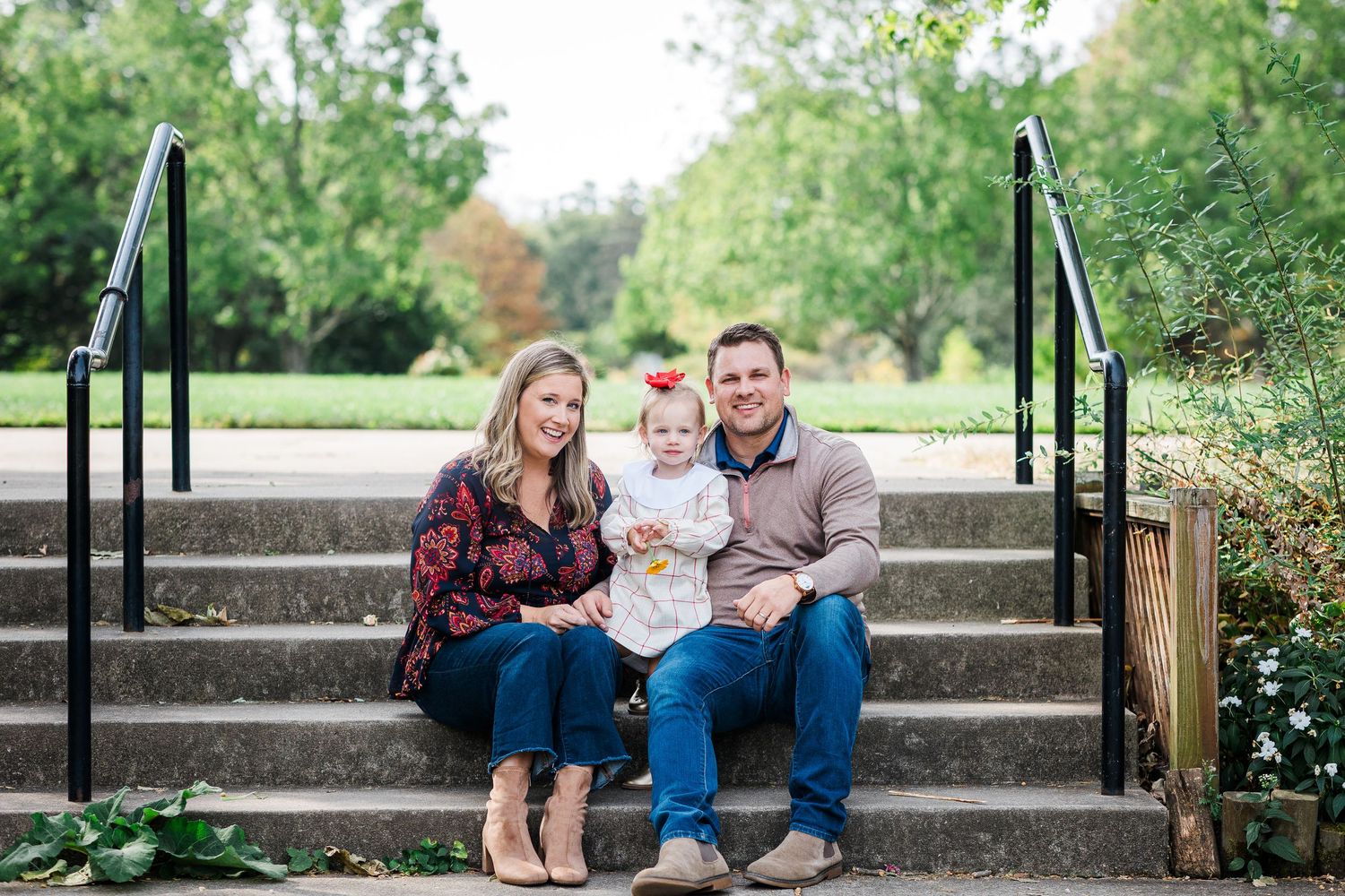 Young family with baby girl sitting on stone steps in park setting.