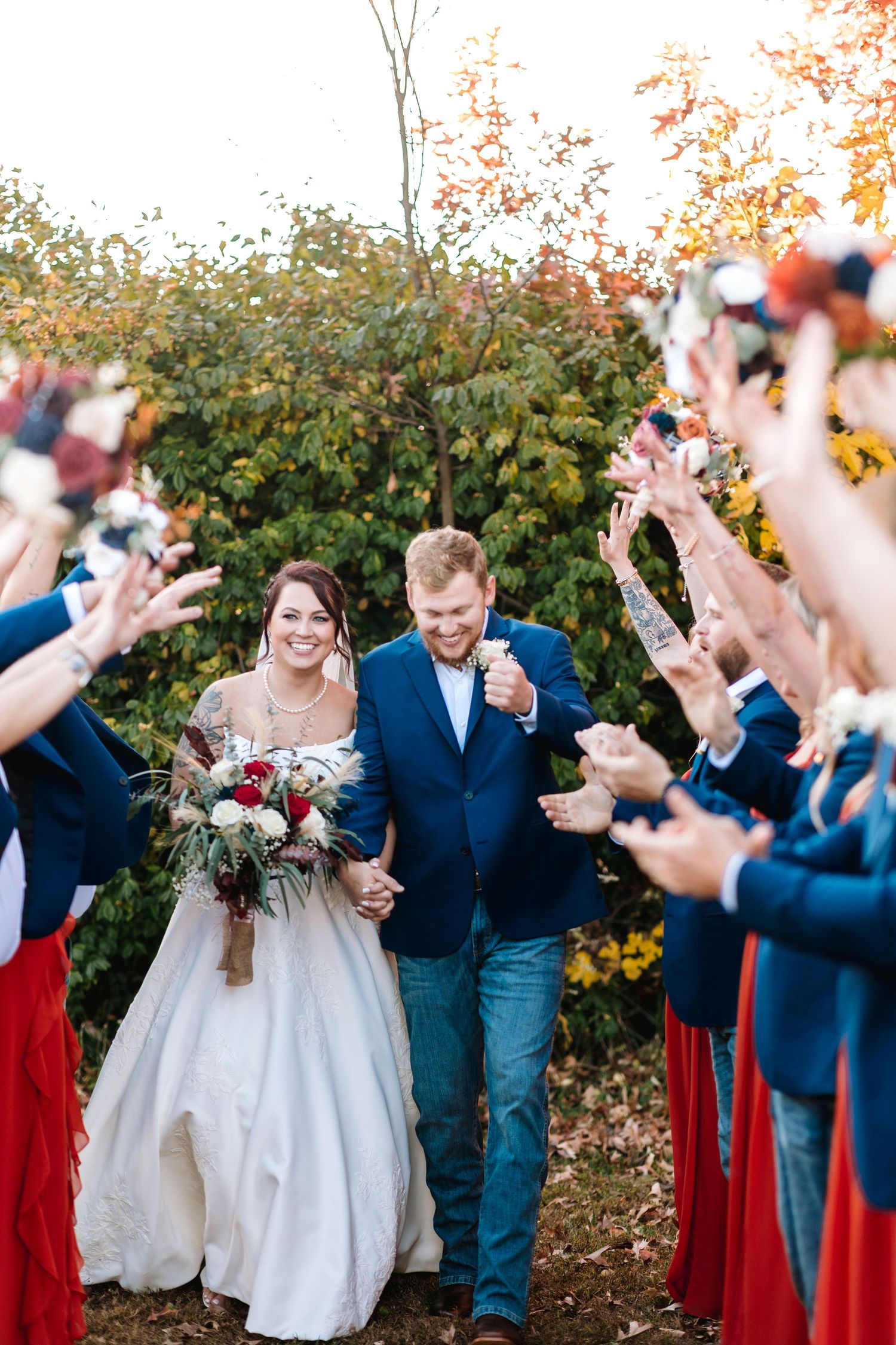 Bride and groom walk through a celebratory tunnel of raised hands during an outdoor fall wedding exit.