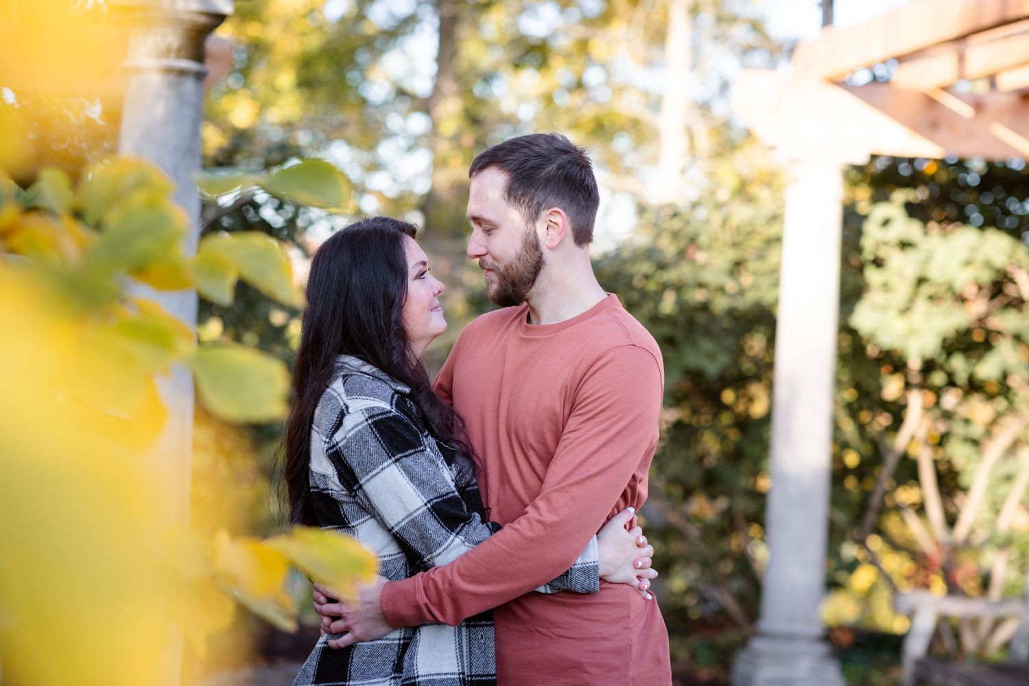 Romantic couple embracing face-to-face surrounded by golden autumn foliage.