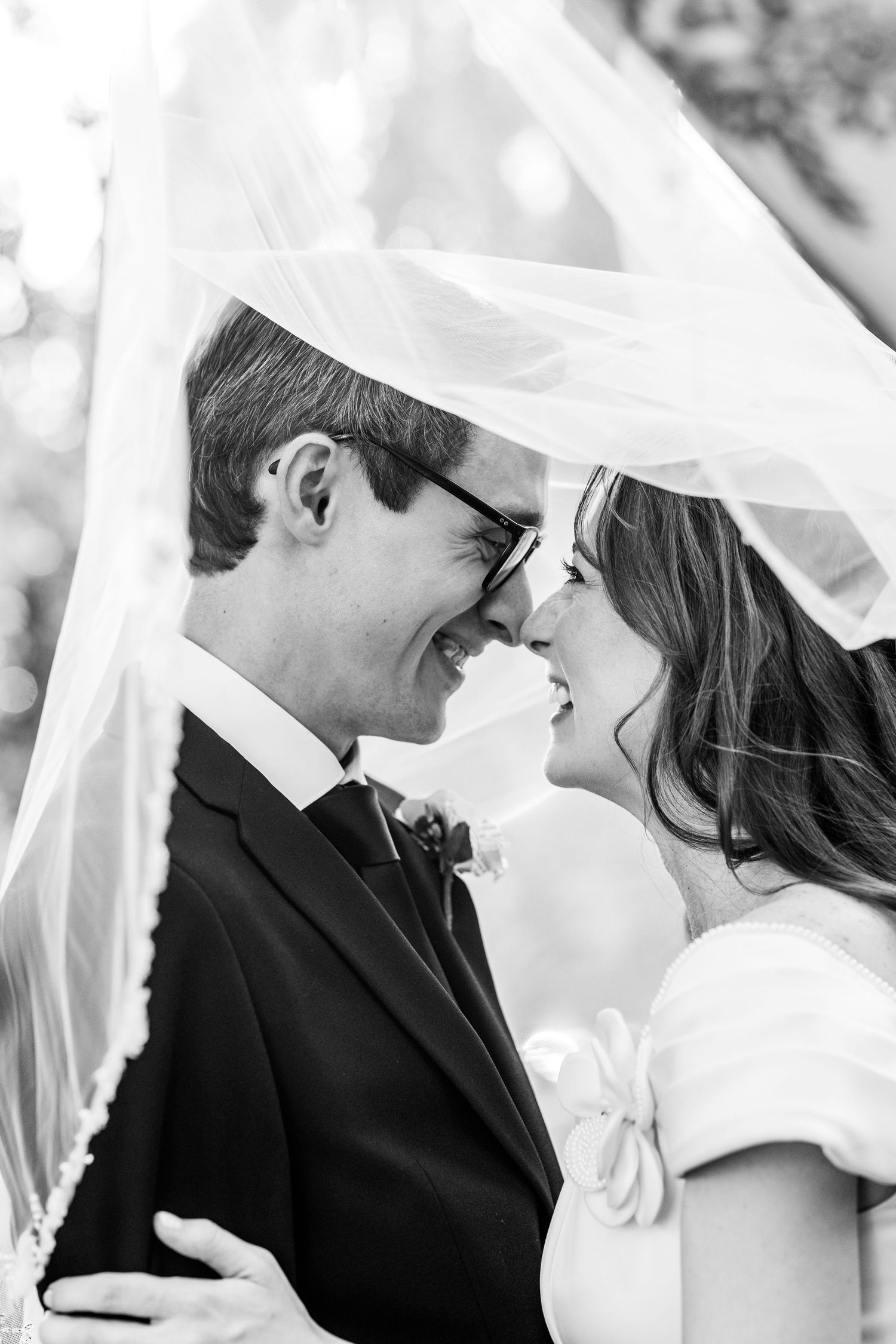 Black and white photo of smiling bride and groom sharing a tender moment under her flowing wedding veil.