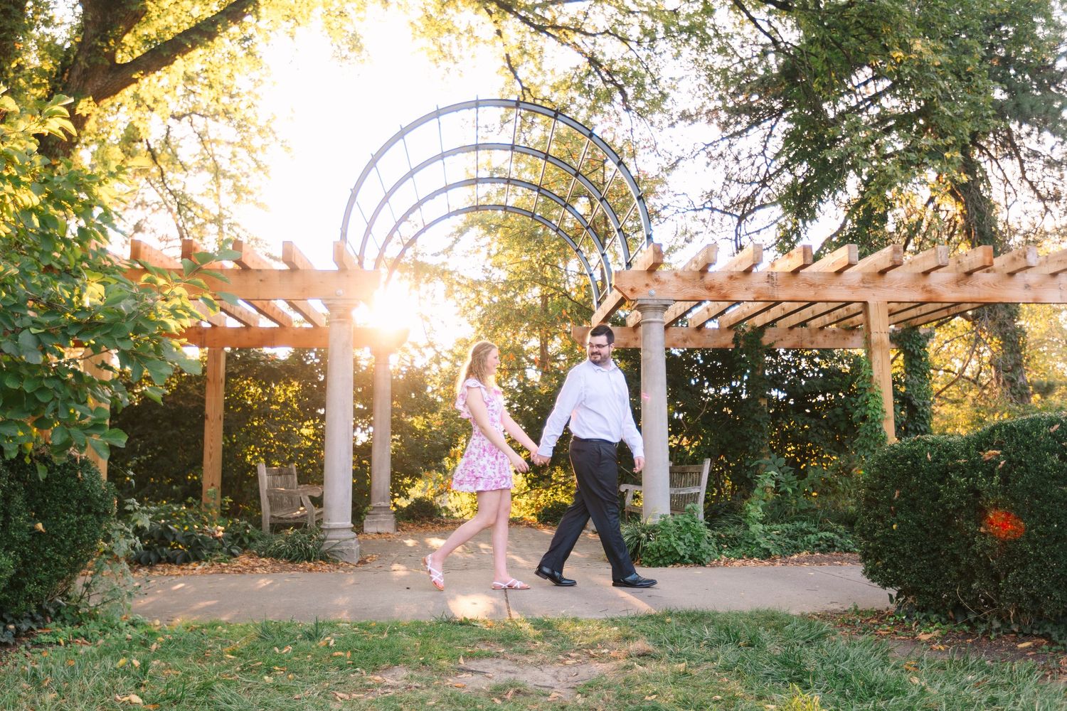 Couple walking hand in hand under a wooden pergola arch at golden hour.