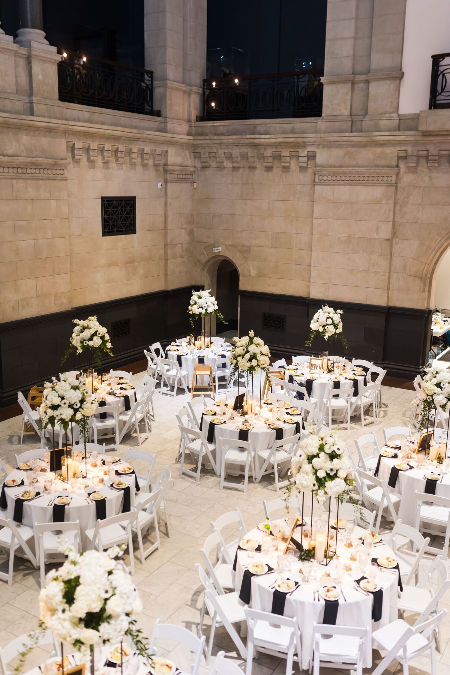 Elegant wedding reception setup at the Cincinnati Art Museum with round tables, white floral centerpieces, and black accents indoors.