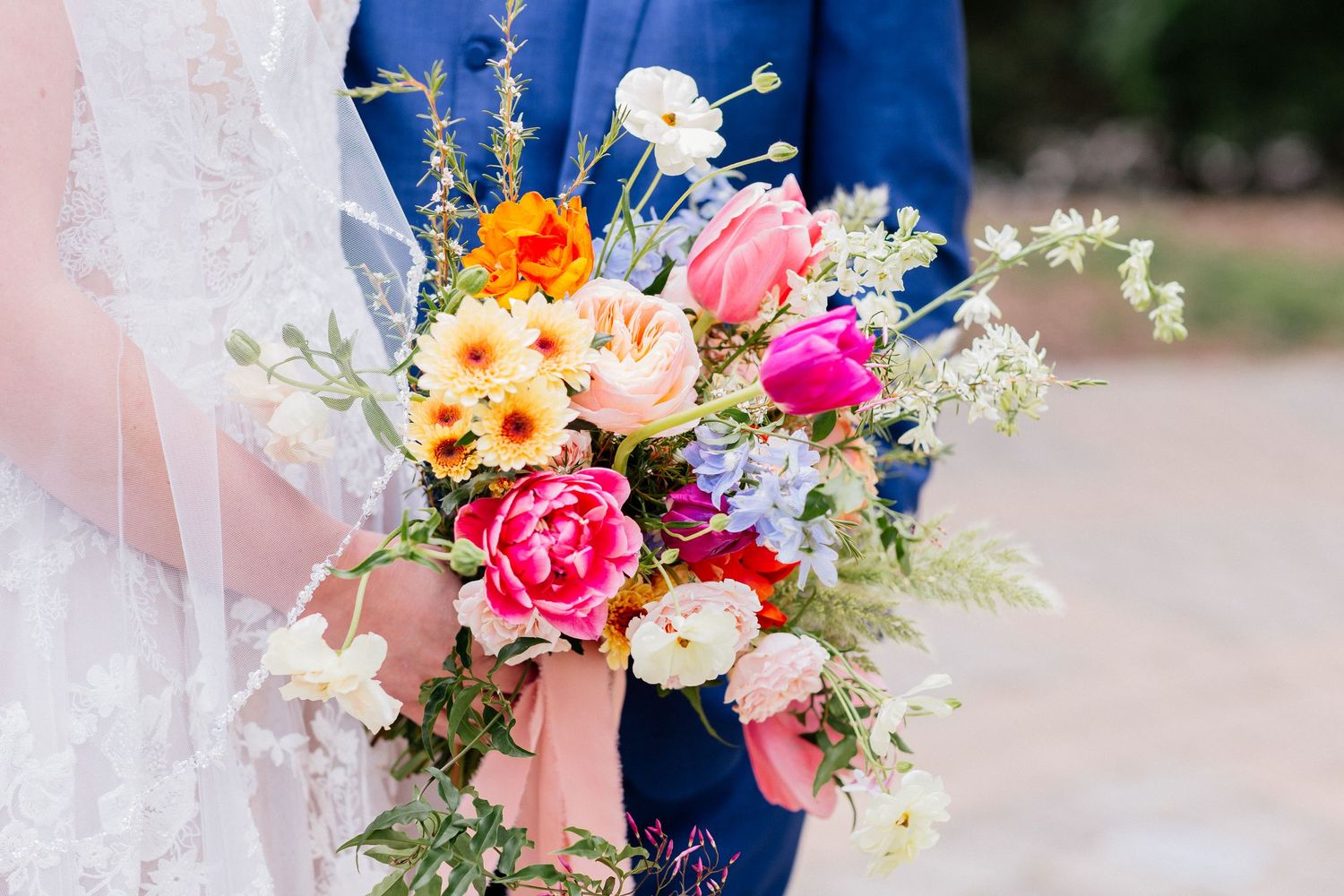 Vibrant bridal bouquet featuring pink peonies, tulips, and wildflowers with a blush ribbon.