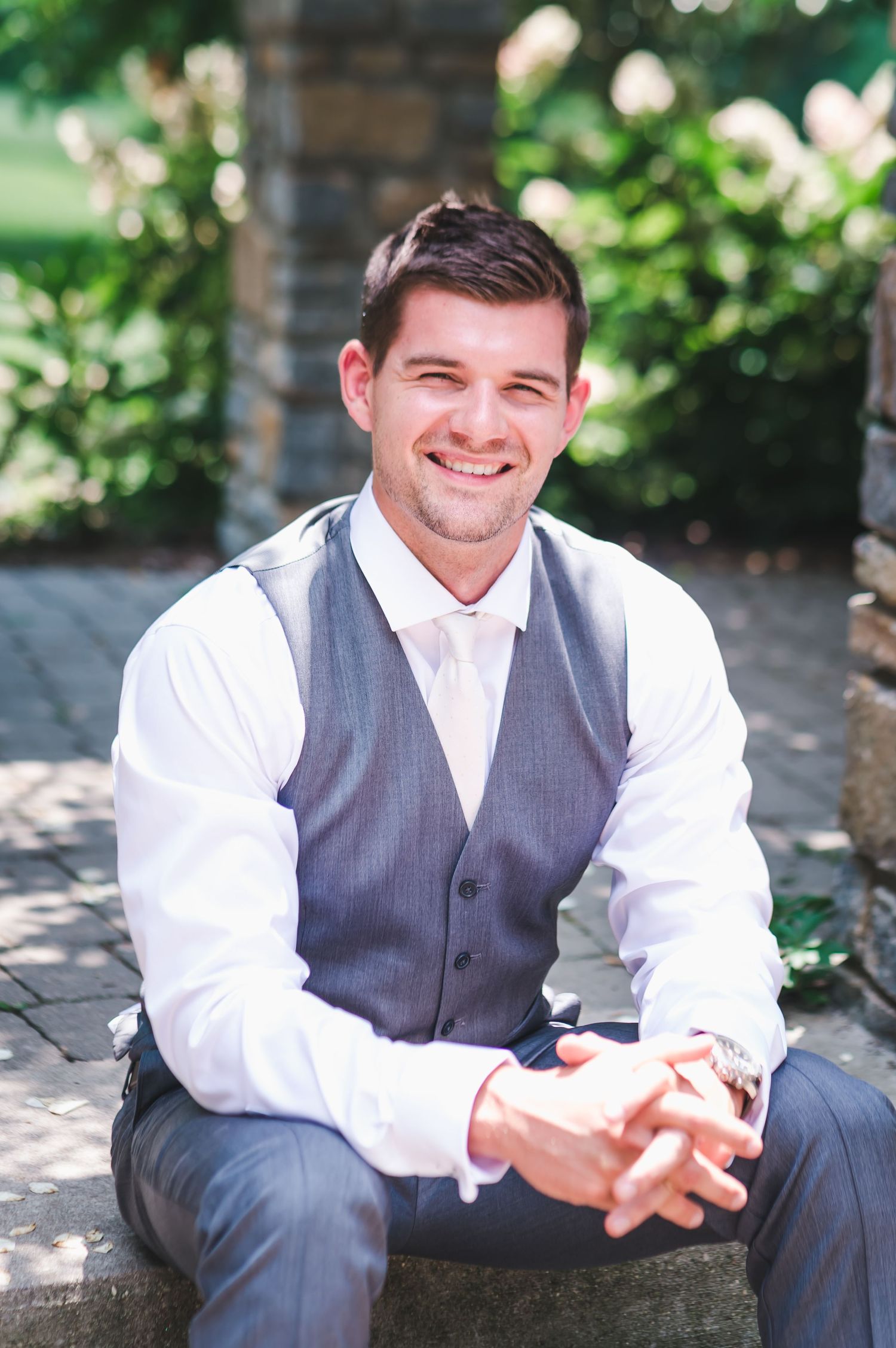 Handsome groom in gray vest and tie smiling outdoors on wedding day.