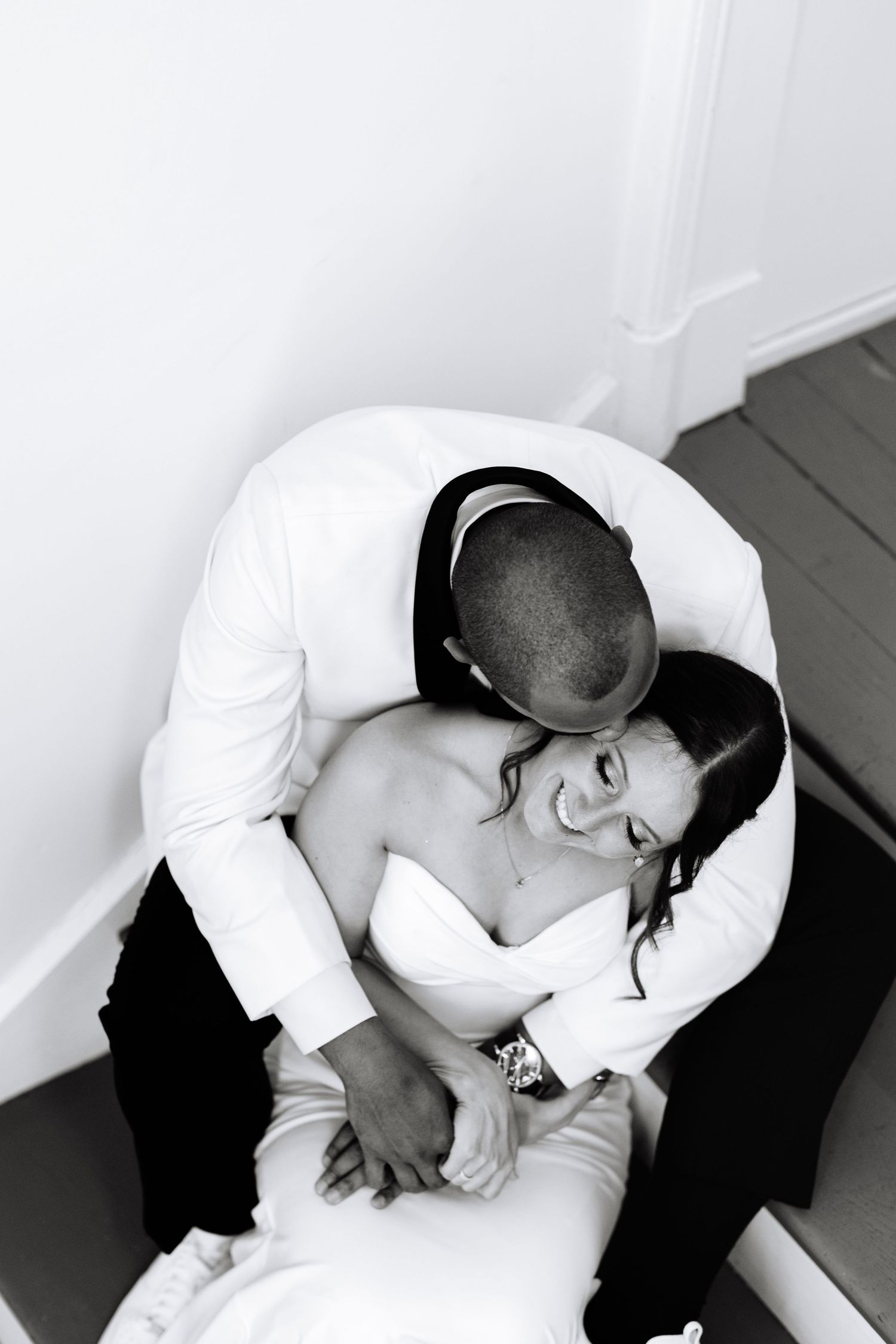 Black and white aerial photo of a groom embracing his smiling bride on a staircase landing at The Alcove by Madtree.