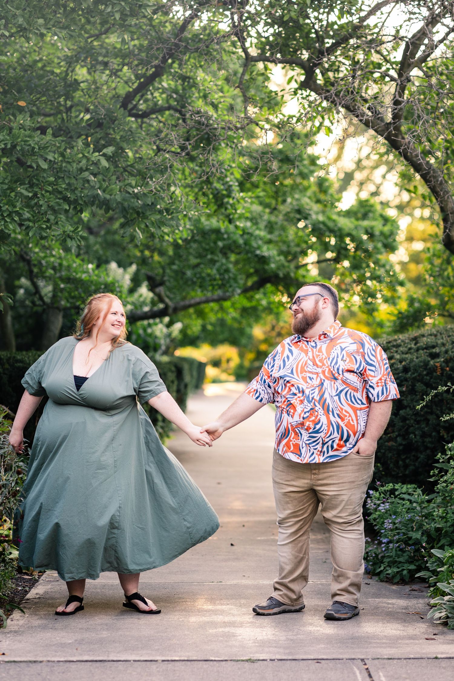 Couple holding hands and walking along a garden path surrounded by lush greenery.