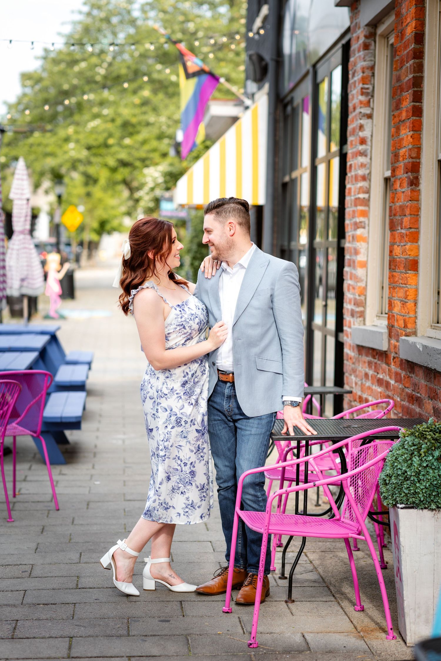 Couple sharing a romantic moment on a colorful urban sidewalk cafe patio with pink chairs nearby.