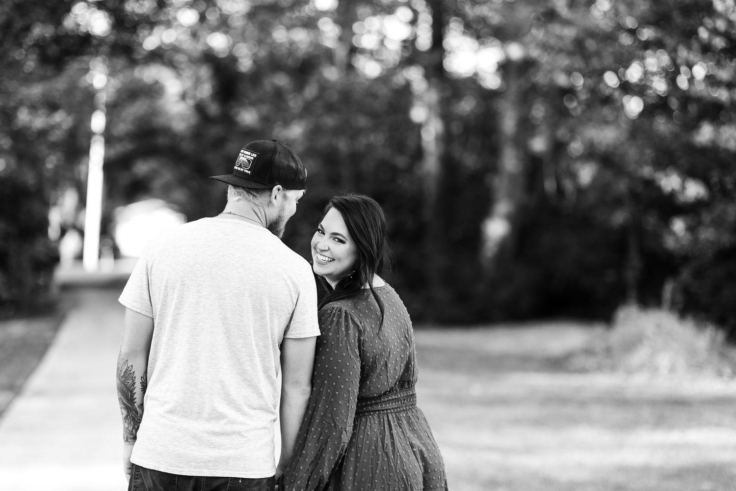 A black and white photo of a couple walking together on a path surrounded by trees.