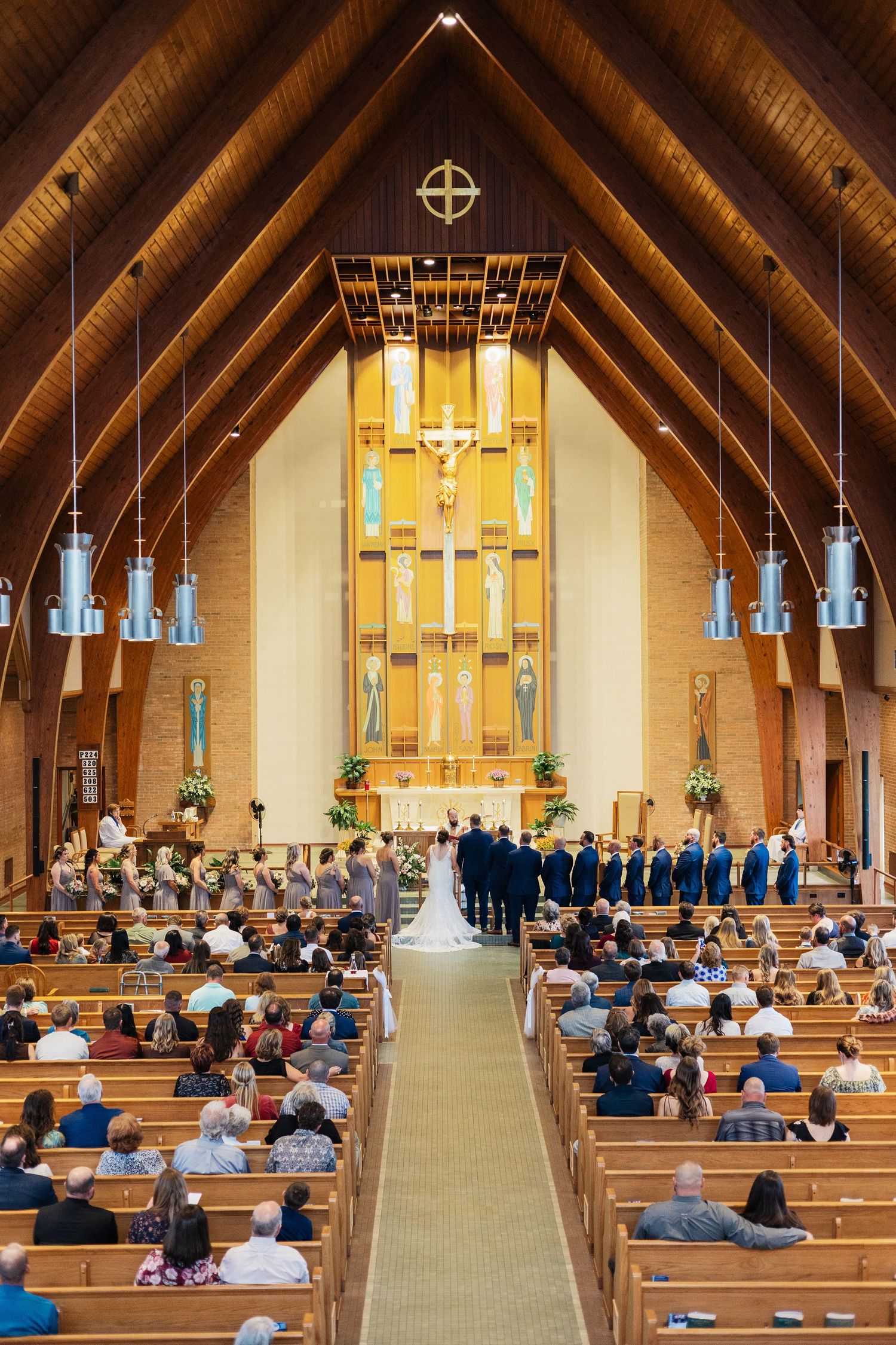 Wedding ceremony inside a beautiful wooden A-frame Catholic church with guests seated in pews.