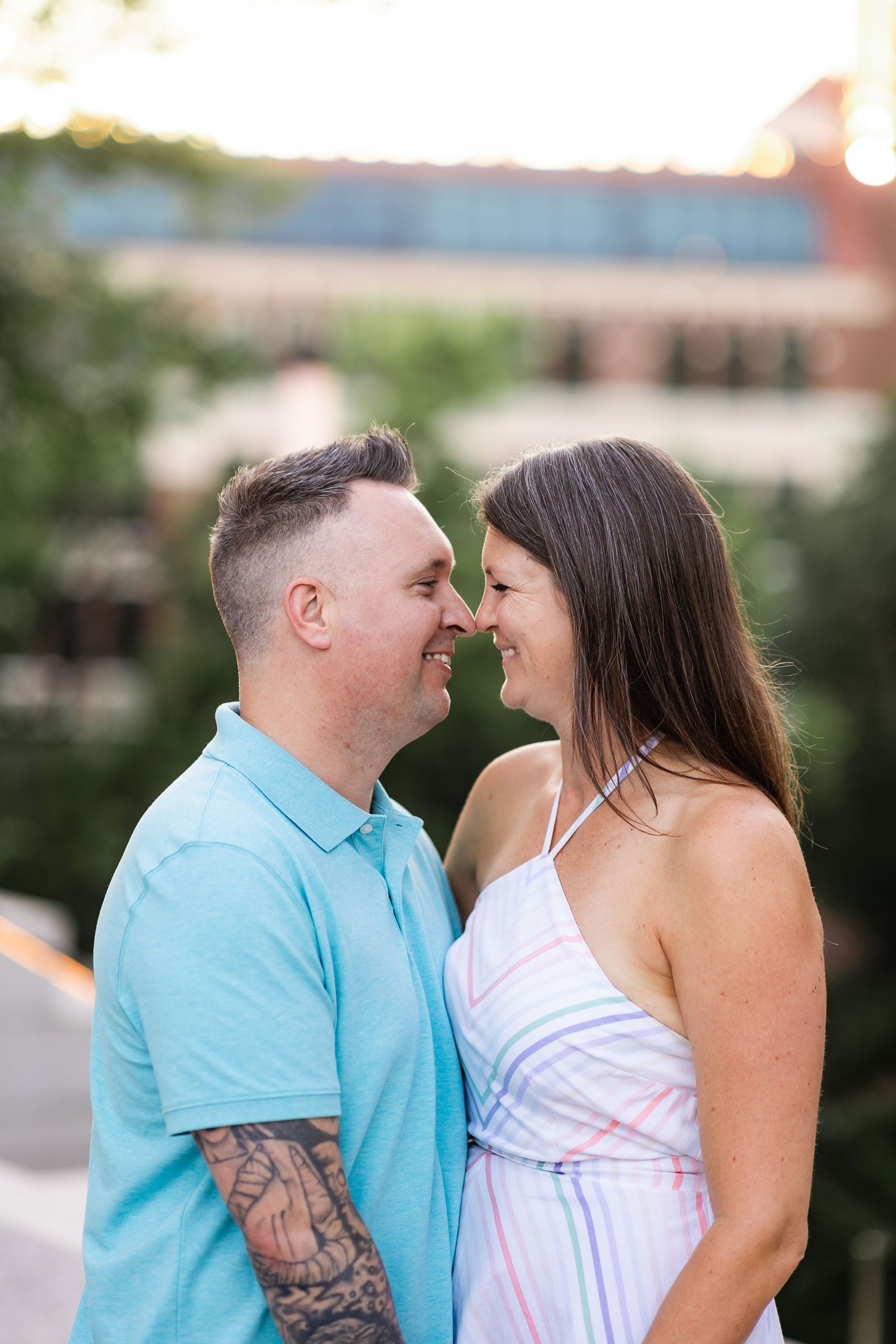 Couple sharing an intimate nose-to-nose moment outdoors with a tattooed man in a teal polo shirt.