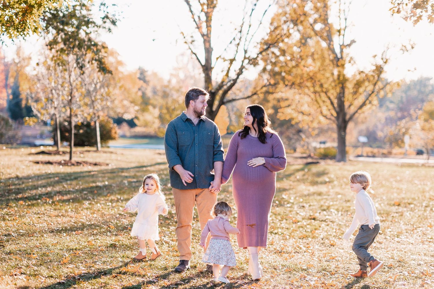 Pregnant mother and father walking with three young children through a sunny autumn park.