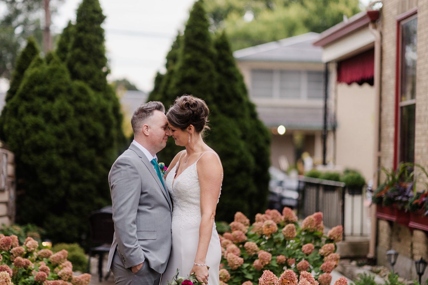 Bride and groom share a romantic moment surrounded by blooming hydrangeas at an outdoor wedding venue.