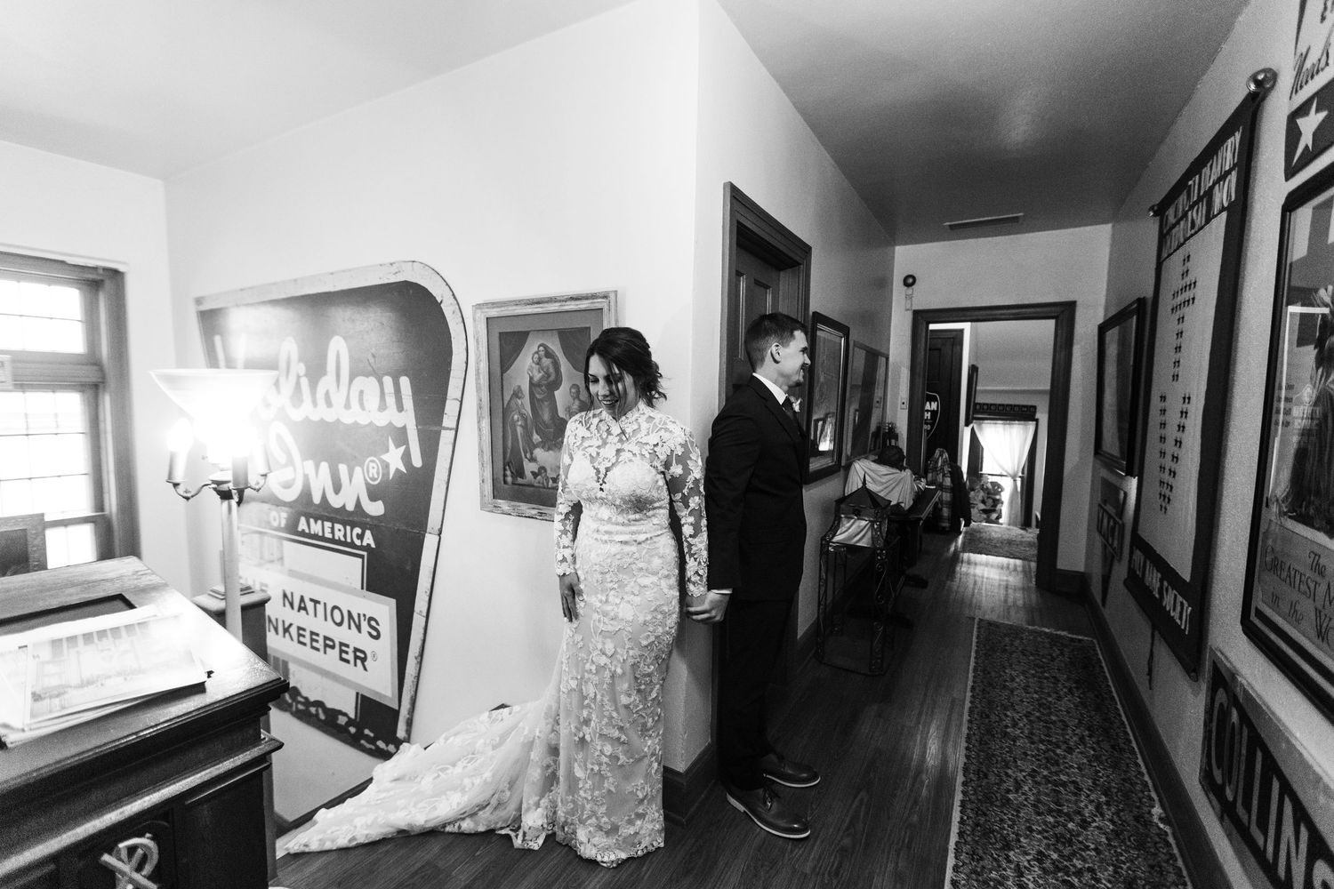 Bride in lace gown and groom share a quiet first look moment in a vintage hallway with retro signage.