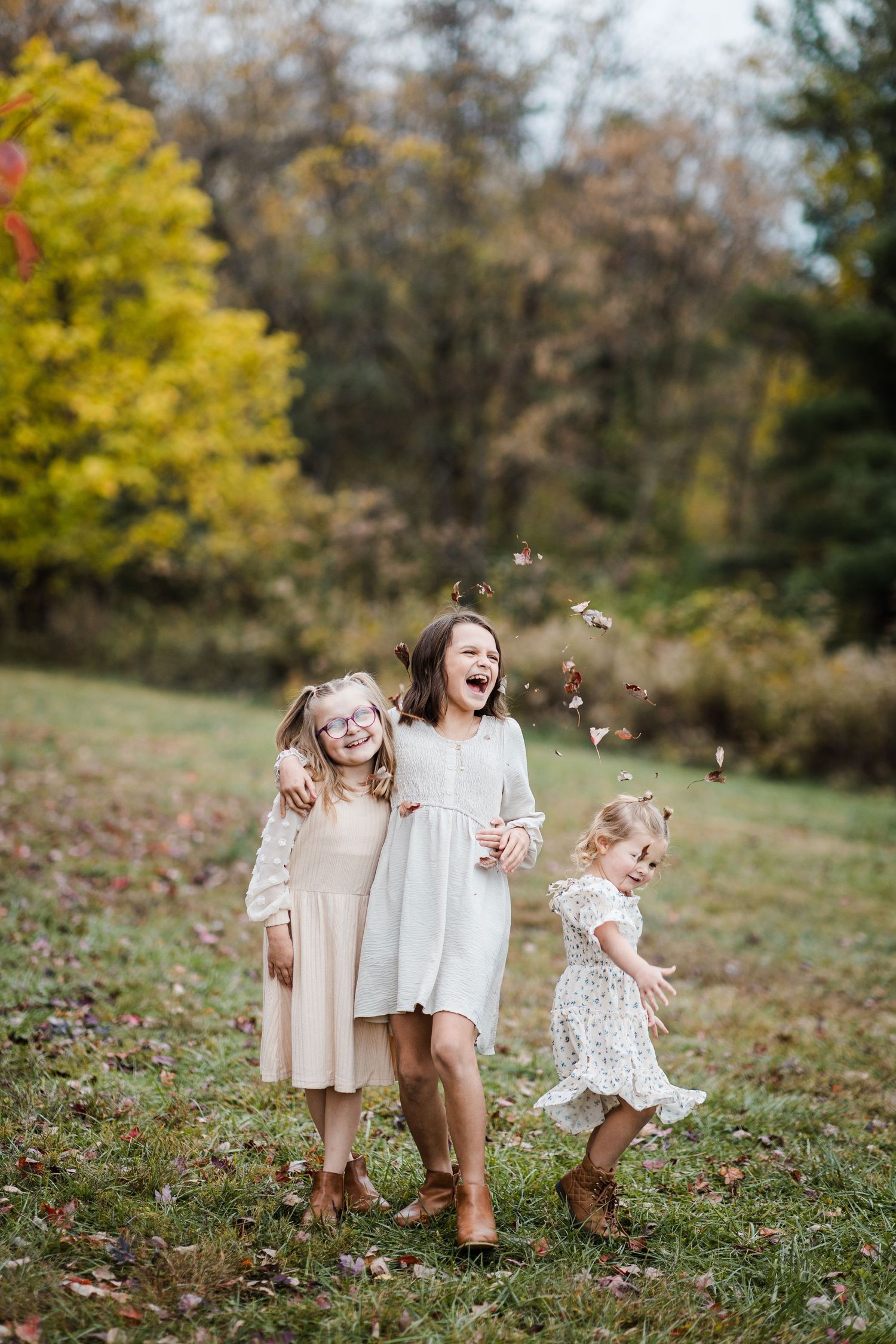Sisters laughing while tossing leaves in French park.