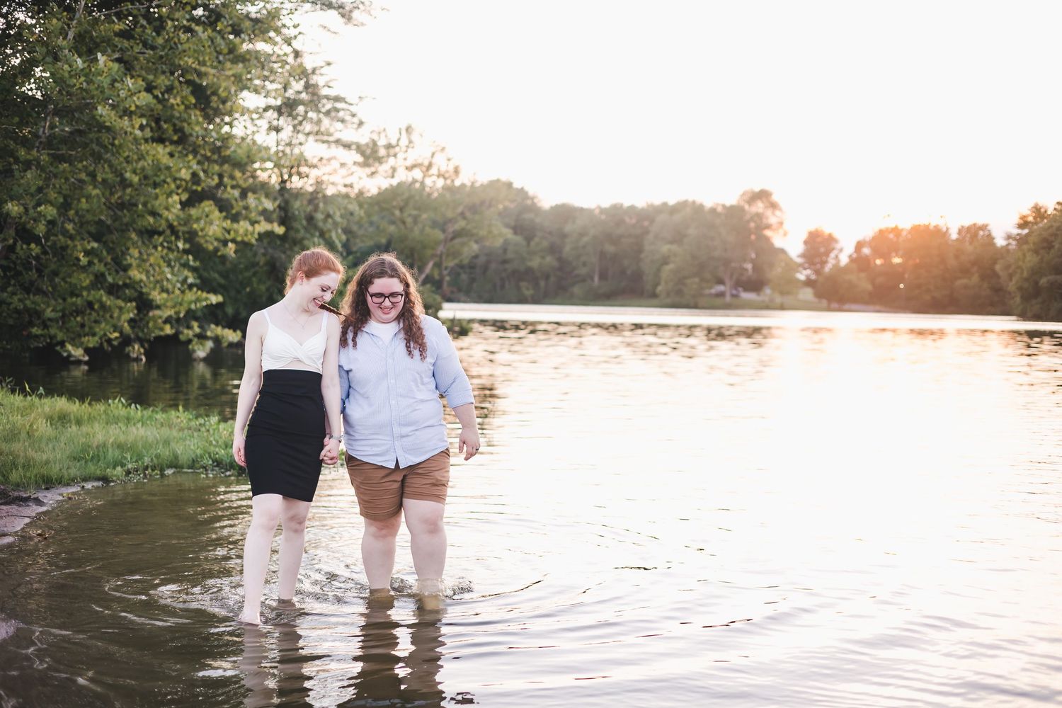Two women holding hands wading through a lake at golden hour sunset.