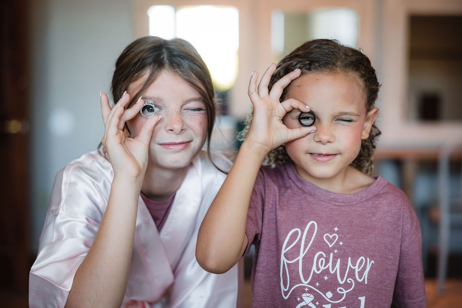 Two young flower girls playfully peek through wedding rings.