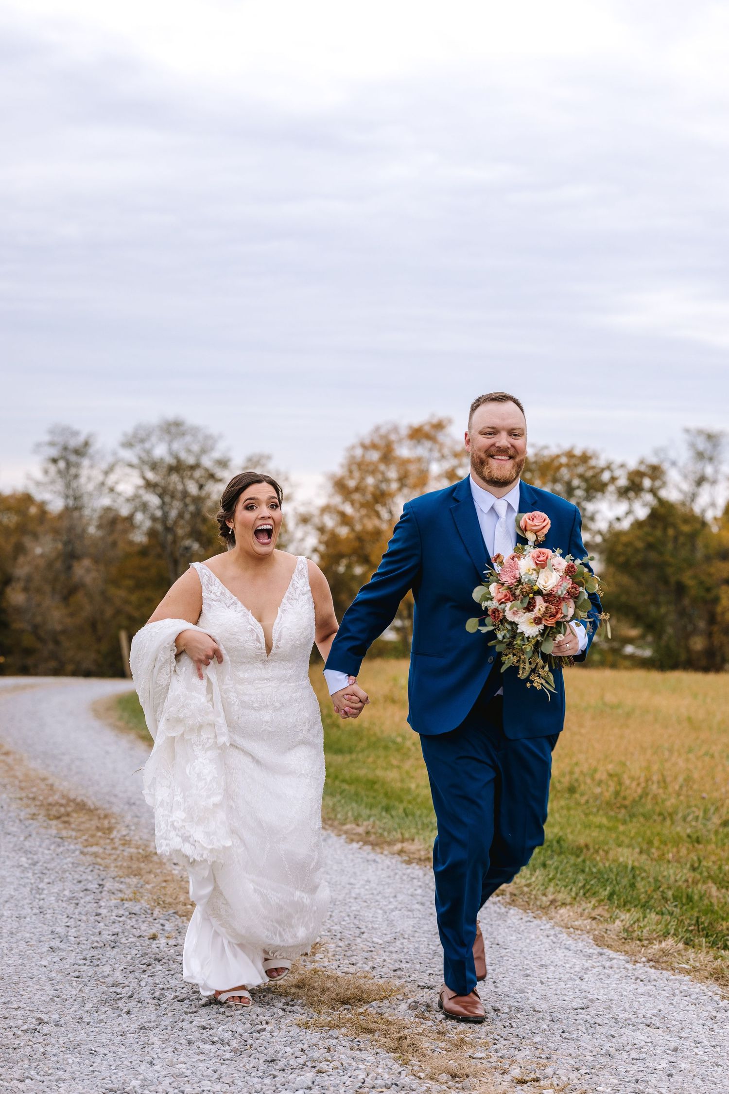 Joyful bride and groom holding bouquet walking hand in hand down a gravel path.