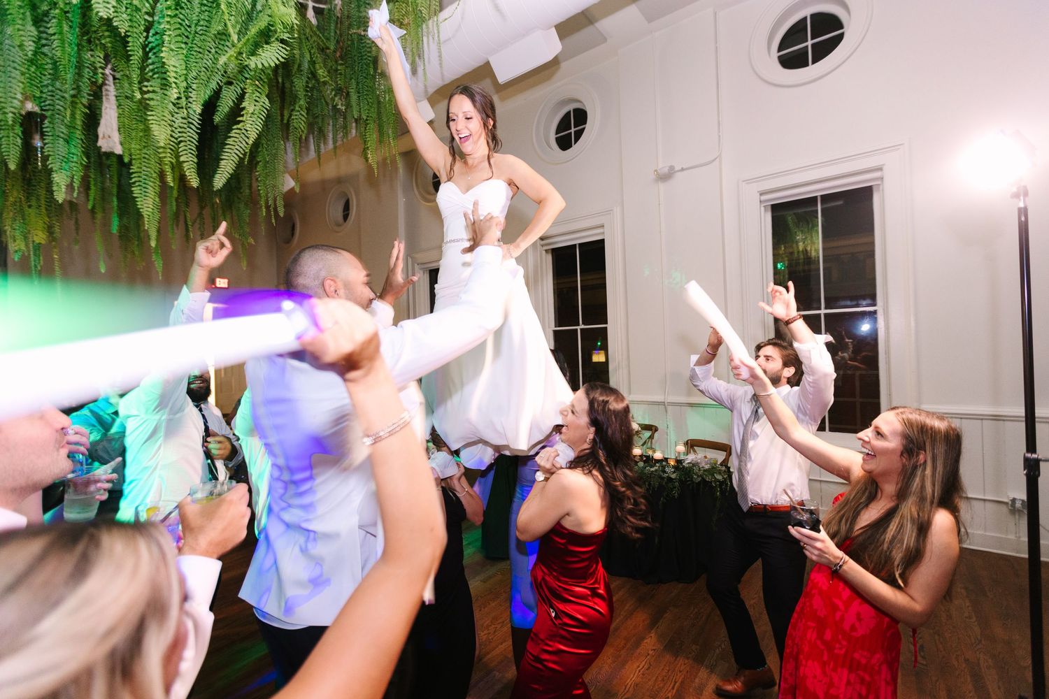 Bride lifted by guests during energetic wedding reception dance party with colorful glow sticks at the Alcove by Madtree.