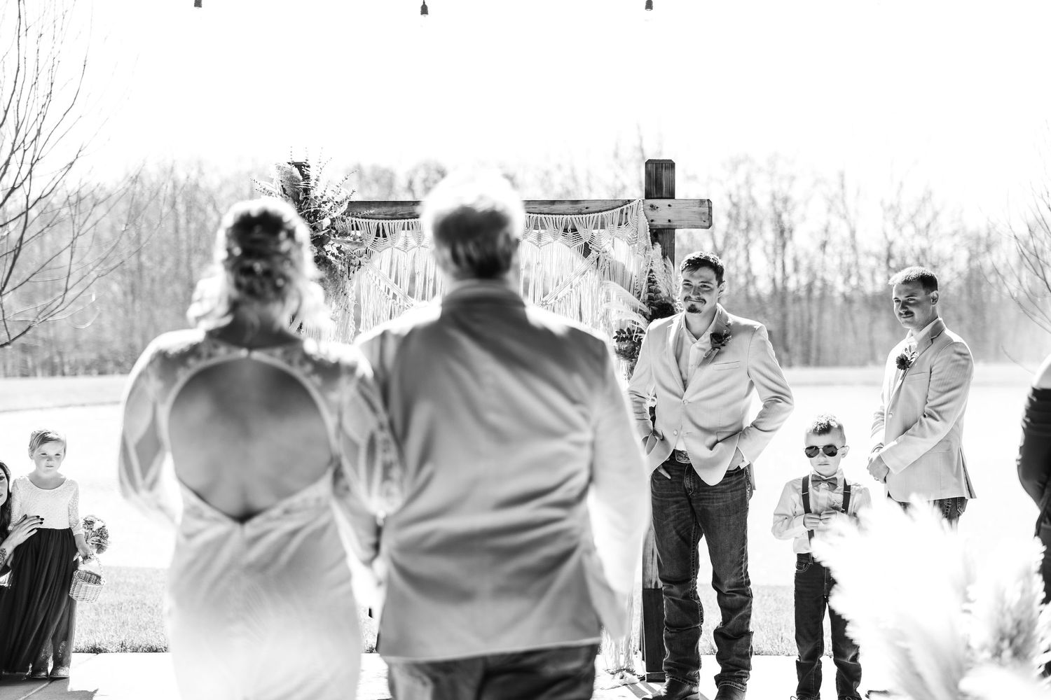 Groom watches bride walk down outdoor aisle with guests seated at Hanover Reserve.