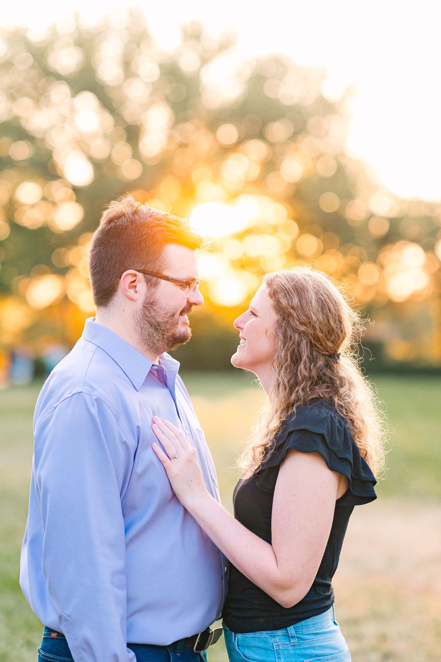 Couple smiling at each other with glowing golden sunset bokeh background.