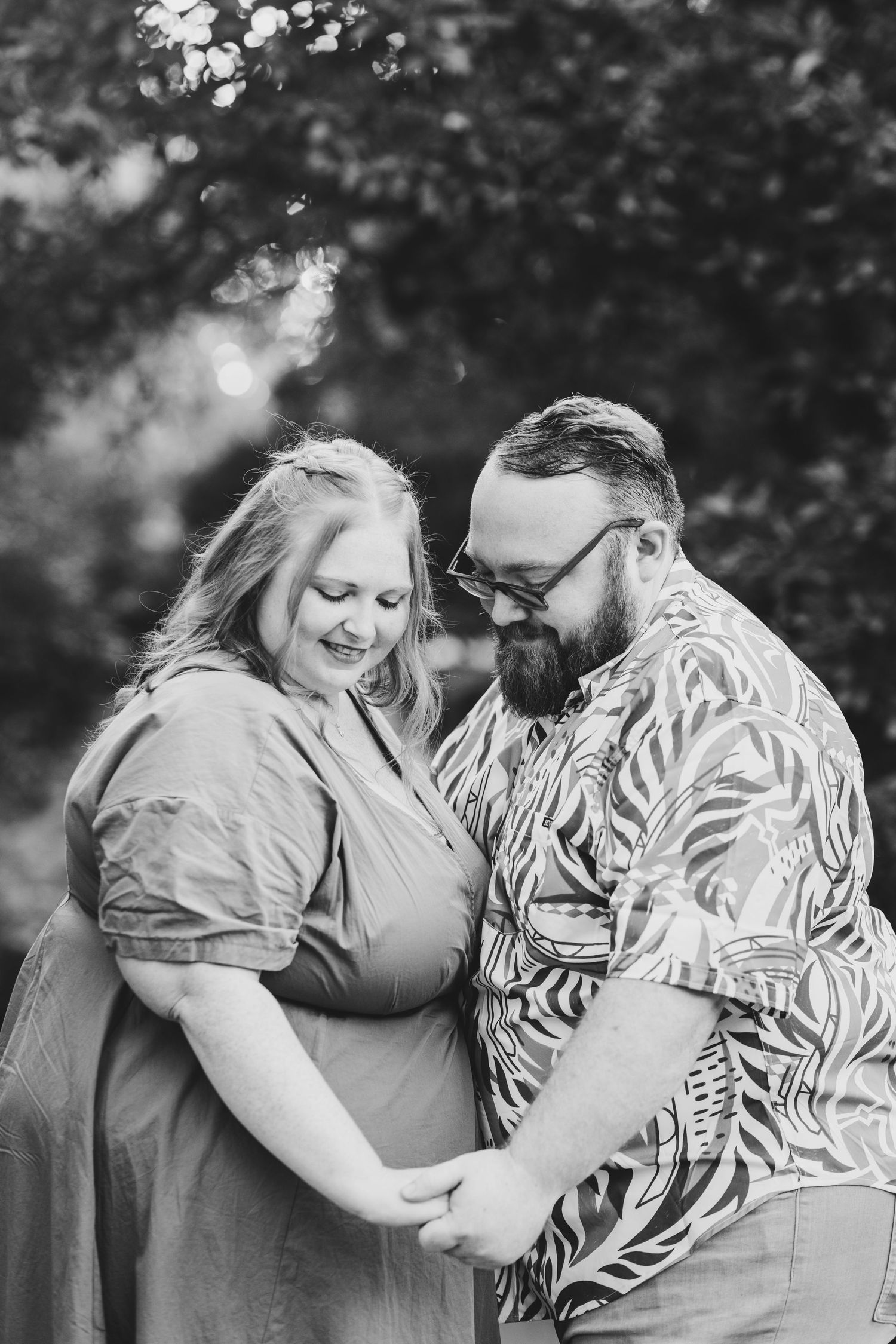 Black and white photo of a couple holding hands and smiling at each other outdoors.