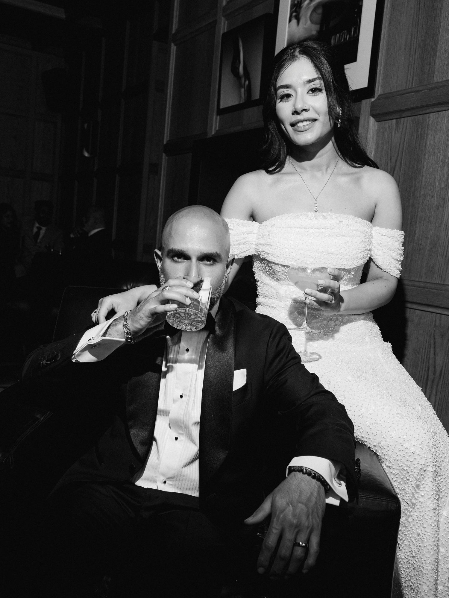 Stylish black and white reception portrait of a bride in a white gown and a groom in a tuxedo enjoying cocktails in the London Edition